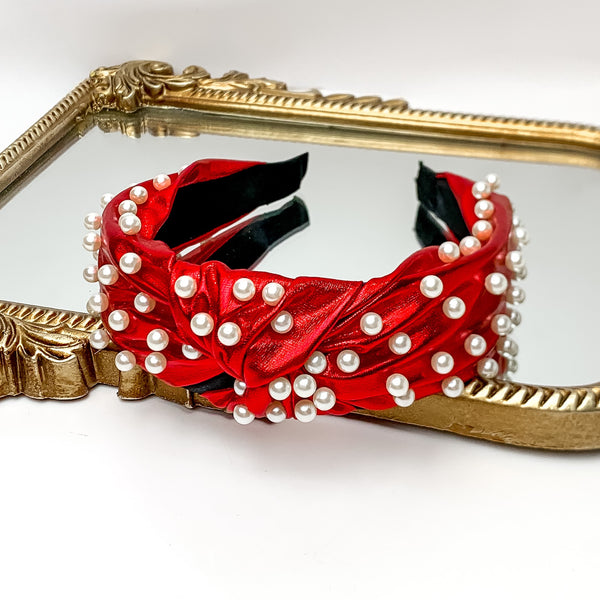Pearl Detailed Knot Headband in Red. Pictured on a white background with the headband on a gold trimmed mirror.
