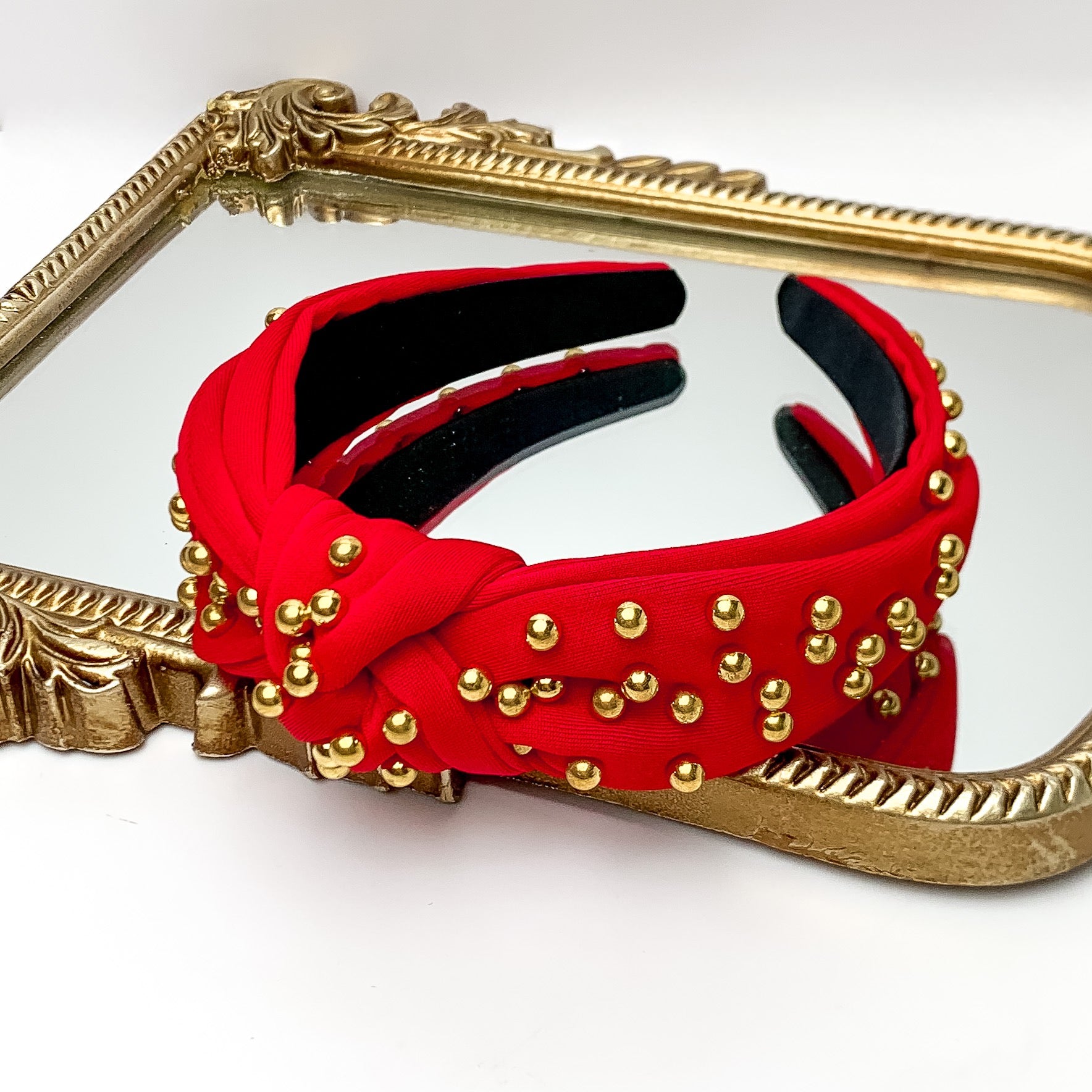 Gold Detailed Knot Headband in Red. Pictured on a white background with the headband on a gold trimmed mirror.