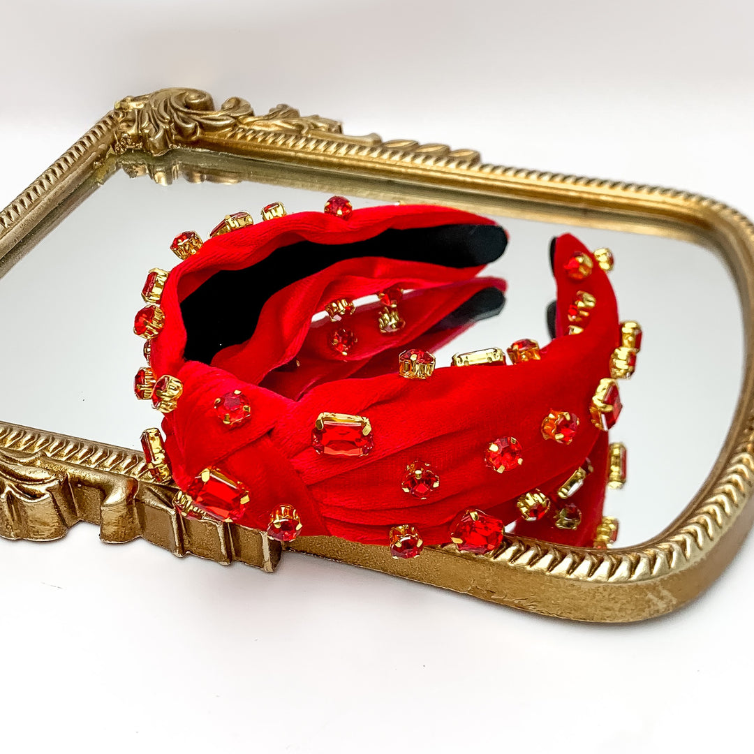 Crystal Detailed Velvet Knot Headband in Red. Pictured on a white background with the headband on a gold trimmed mirror.