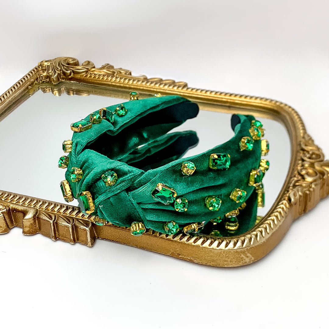 Crystal Detailed Velvet Knot Headband in Emerald Green. Pictured on a white background with the headband on a gold trimmed mirror.