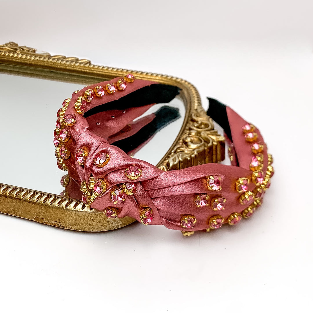 Crystal Detailed Satin Knot Headband in Rose Pink. Pictured on a white background with the headband on a gold framed mirror.