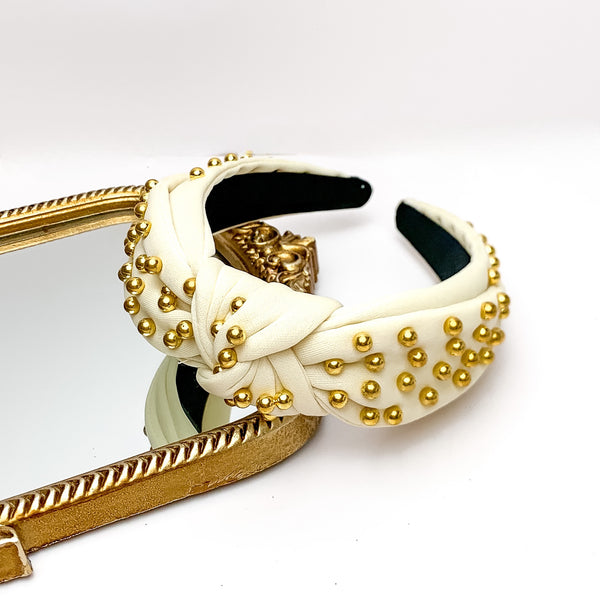 Gold Detailed Knot Headband in Ivory. Pictured on a white background with the headband on a gold trimmed mirror.