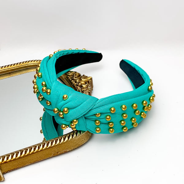 Gold Detailed Knot Headband in Turquoise. Pictured on a white background with the headband on a gold trimmed mirror.