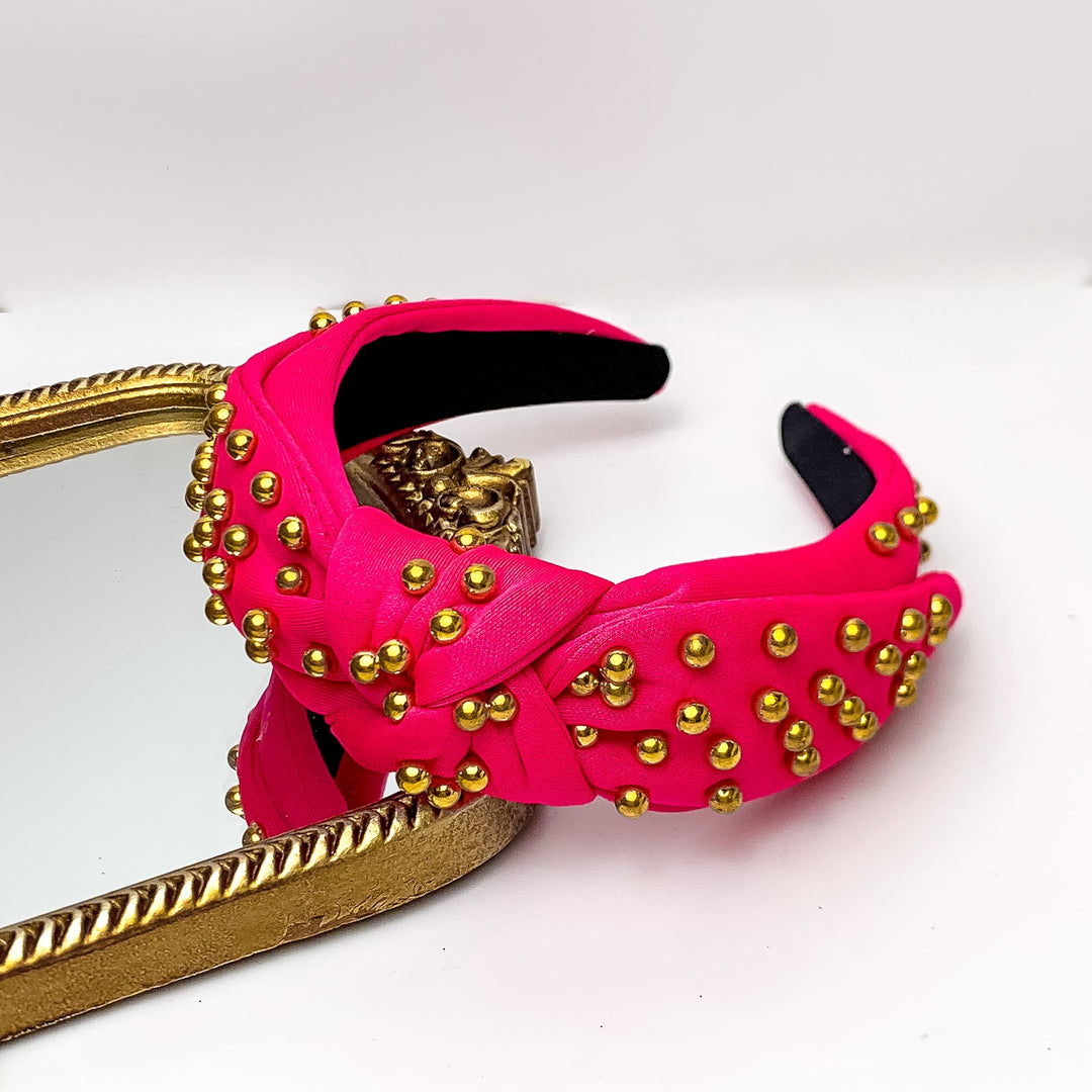 Gold Detailed Knot Headband in Hot Pink. Pictured on a white background with the headband on a gold trimmed mirror.