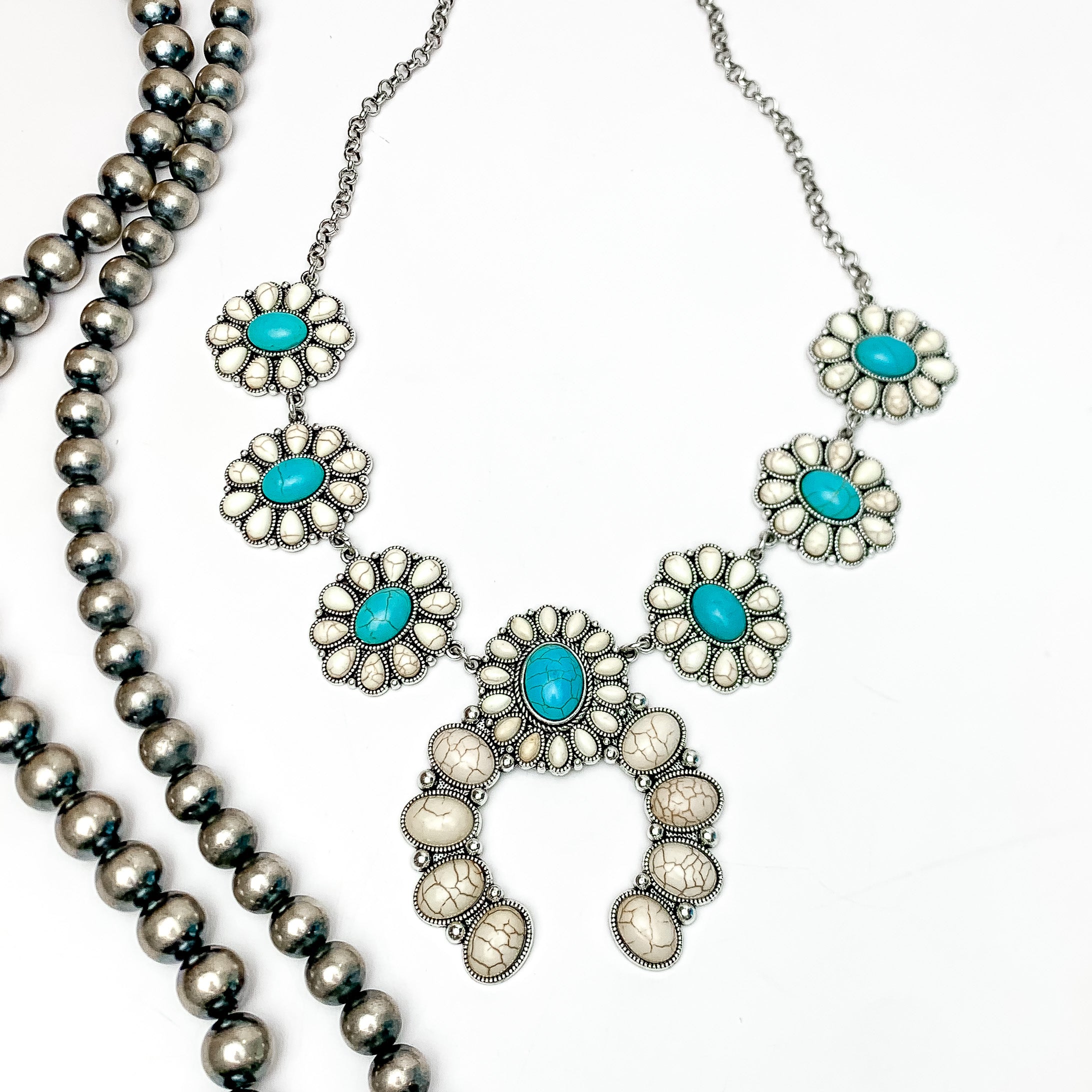 The Western Way Squash Blossom Necklace in Turquoise Blue and Ivory. Pictured on a white background with Navajo beads on the left.