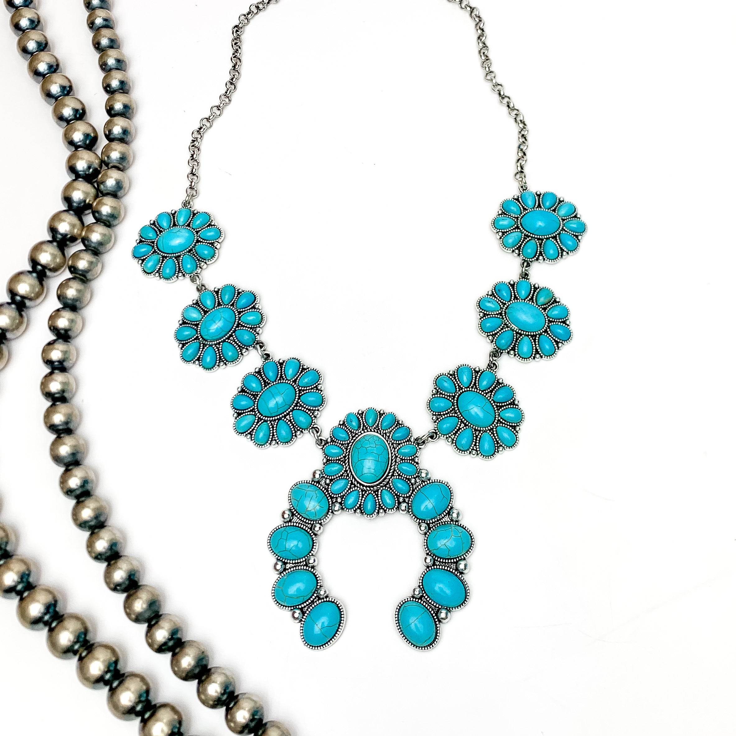 The Western Way Squash Blossom Necklace in Turquoise Blue. Pictured on a white background with Navajo beads on the left.
