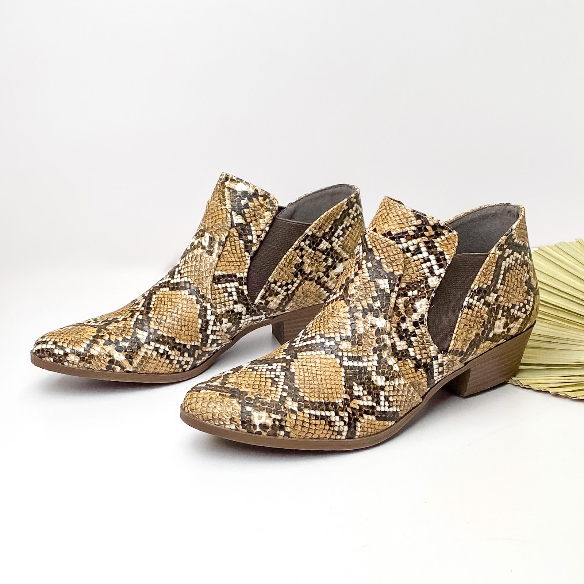 Brown snake print, pointed ankle booties pictured on a white background with a green leaf on the right hand side.