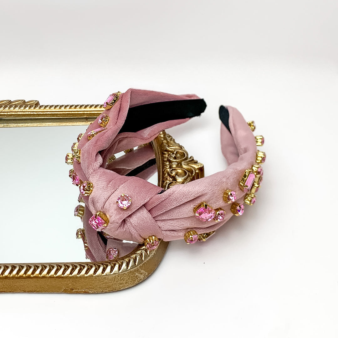 Crystal Detailed Velvet Knot Headband in Mauve Pink. This headband is pictured on a white background with part of the headband on a gold trimmed mirror.