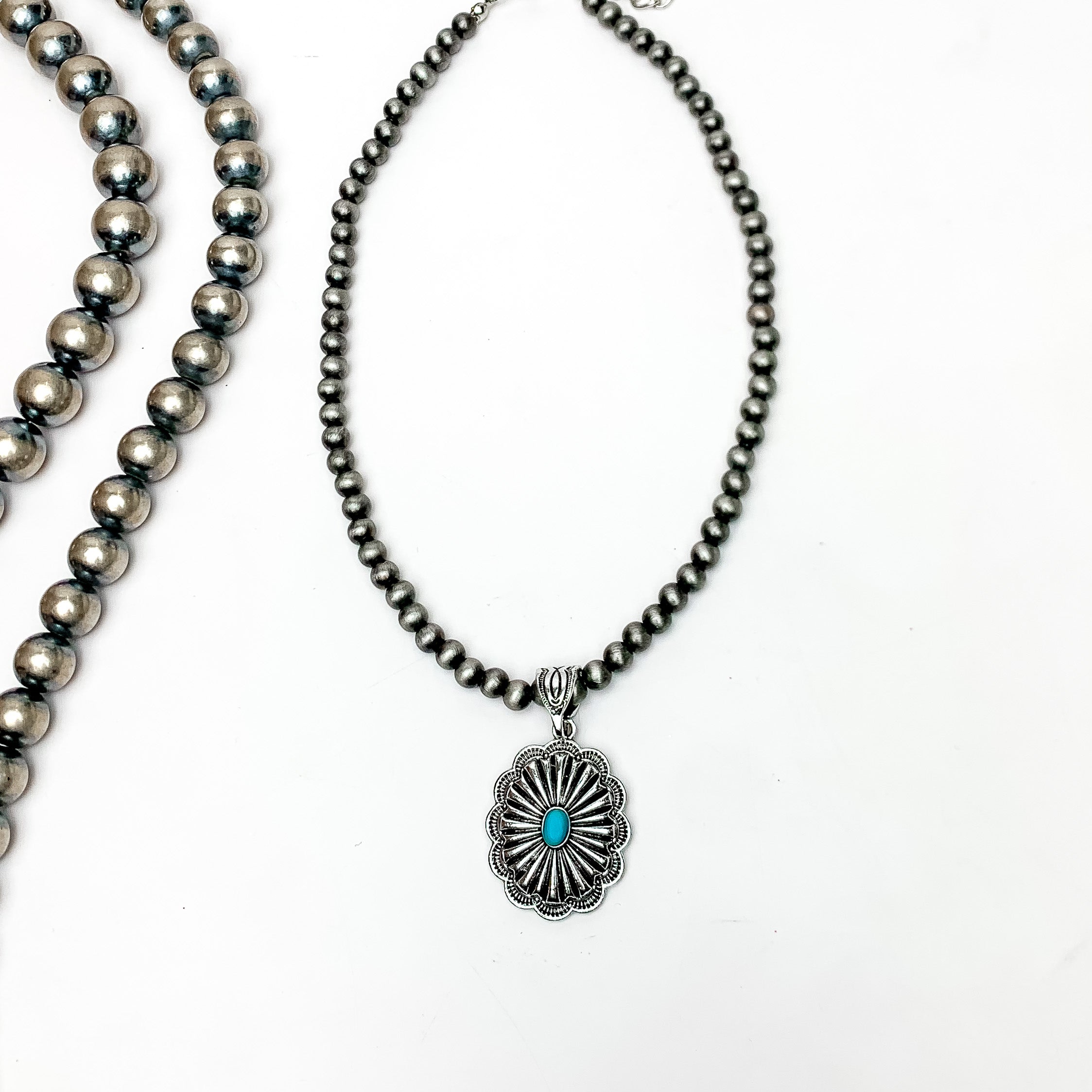 Silver Tone Pearl Necklace Featuring a Pendent With Turquoise Stone. Pictured on a white background with Navajo peals on the left side of the necklace.