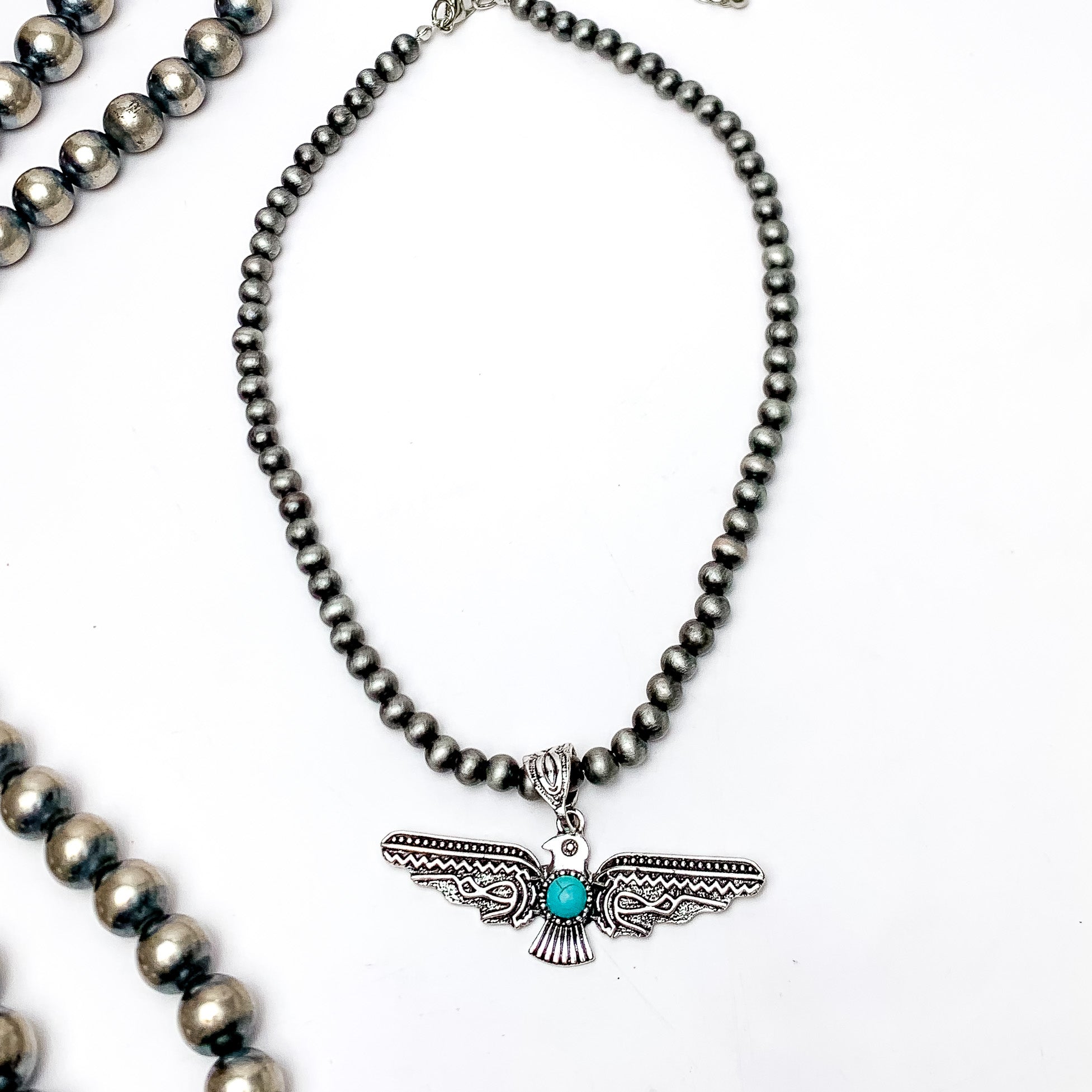 Thunder Bird Pendent Silver Tone Beaded Necklace. This silver beaded necklace with a turquoise stone is pictured on a white background with Navajo beads on the left side.
