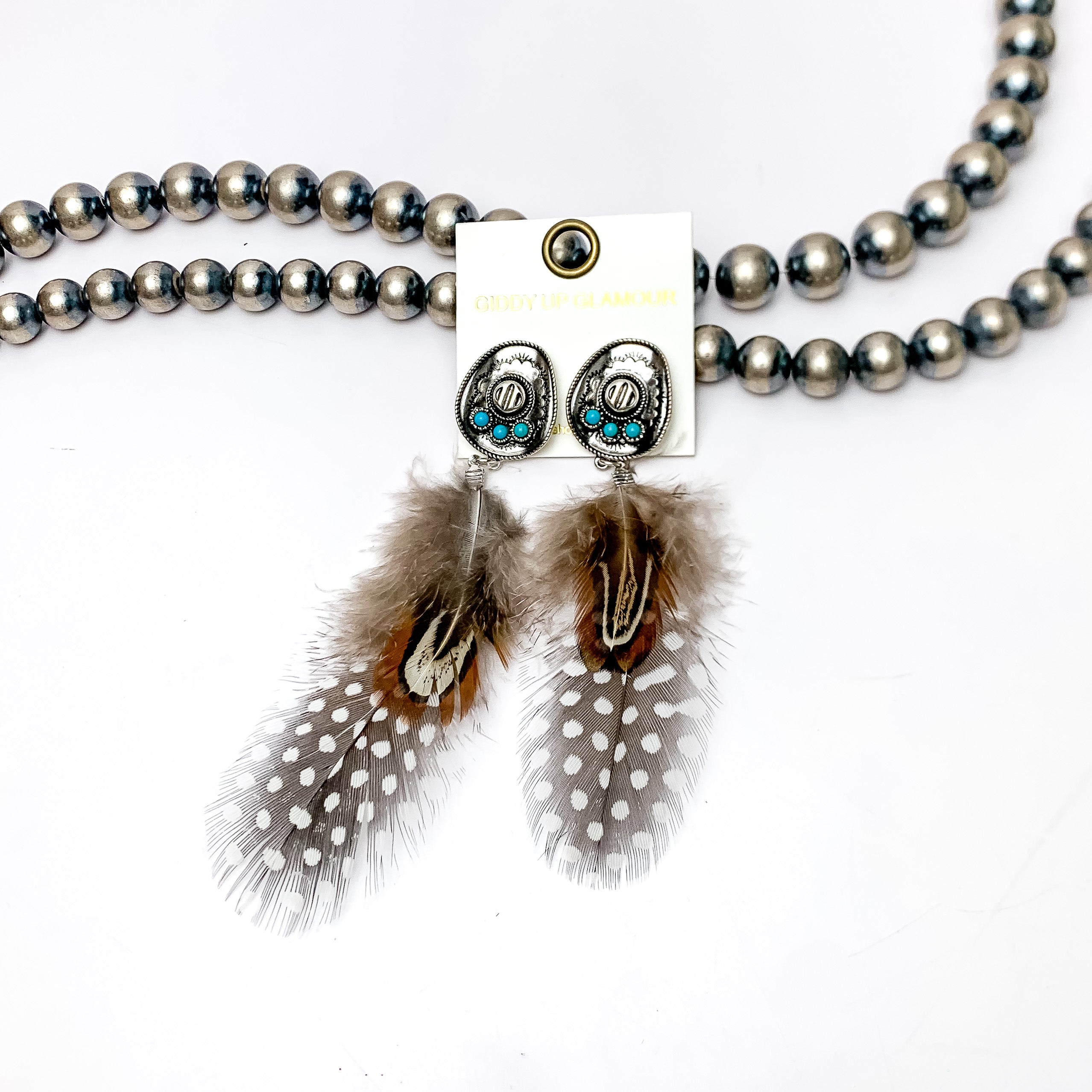 Cowboy Hat Post Feather Earrings in Brown and Black. These Earrings are pictured laying against Navajo pearls with a white background.