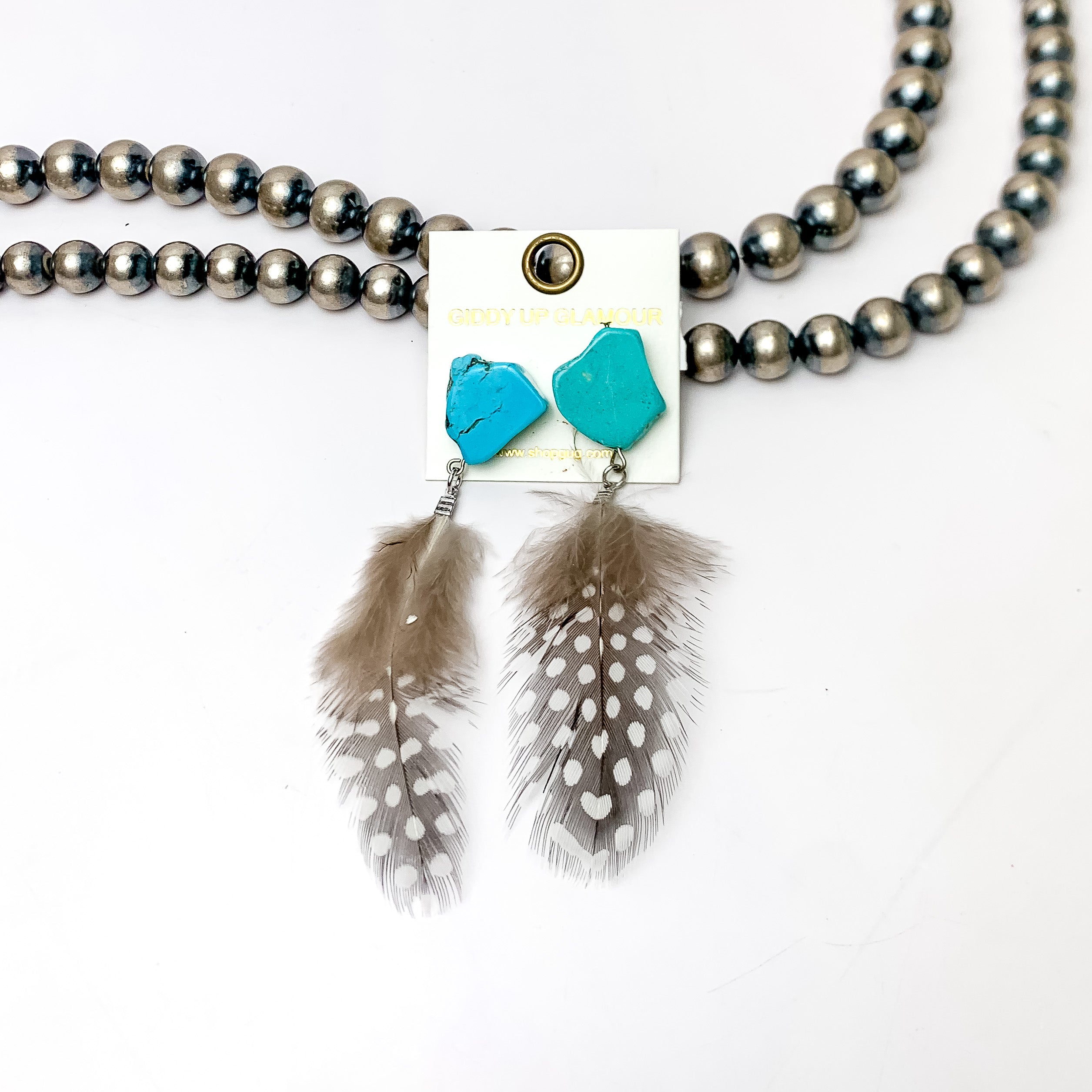 Turquoise Stone Post Feather Earrings in Brown and Black. These Earrings are pictured laying against Navajo pearls with a white background.