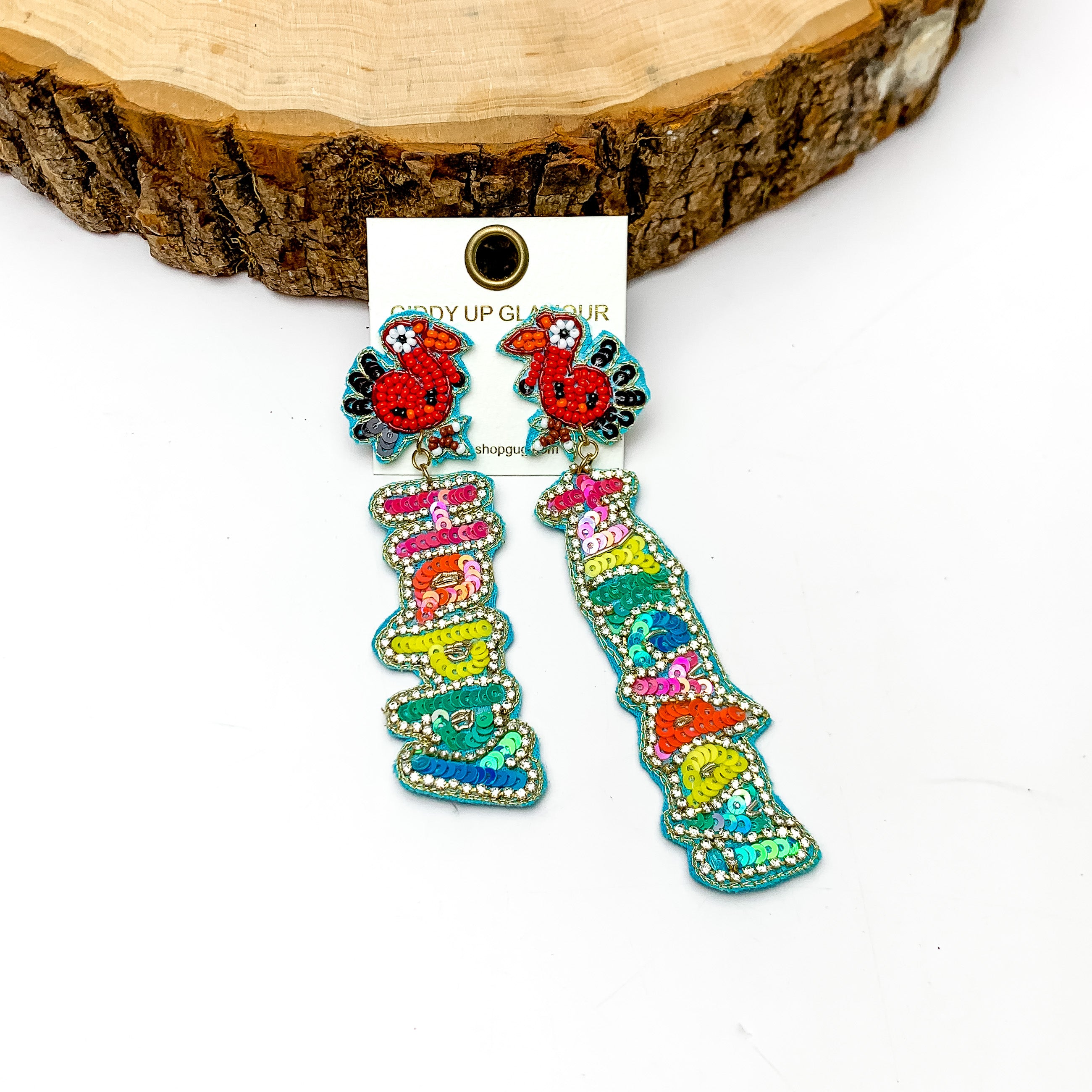 Happy Turkey Day Beaded Earrings in Multicolor. These beaded colorful earrings spell out happy turkey day. They are laying against a piece of wood on a white background.