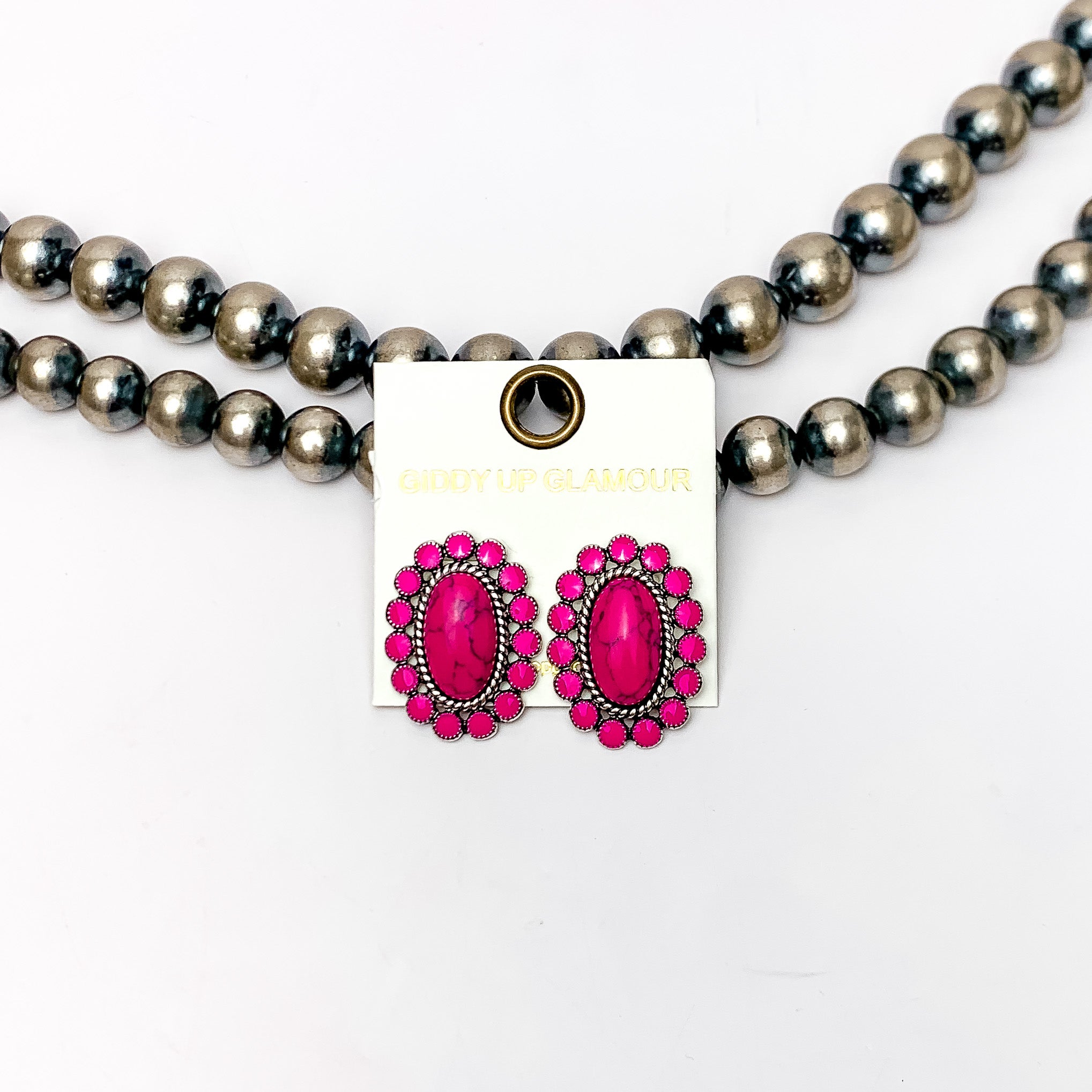 Concho post earrings in hot pink. These earrings are pink stones surrounding a bigger stone. Pictured on a white background with Navajo pearls behind the earrings.