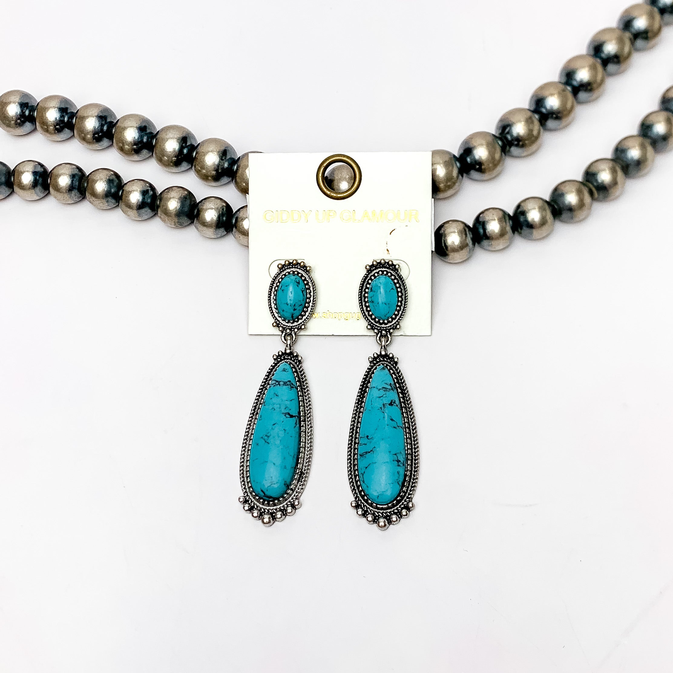 Southern Saturdays Silver Tone Drop Earrings in Turquoise Blue. These earrings featured two large stones. The background of the picture is white and the earrings are laying against Navajo pearls.