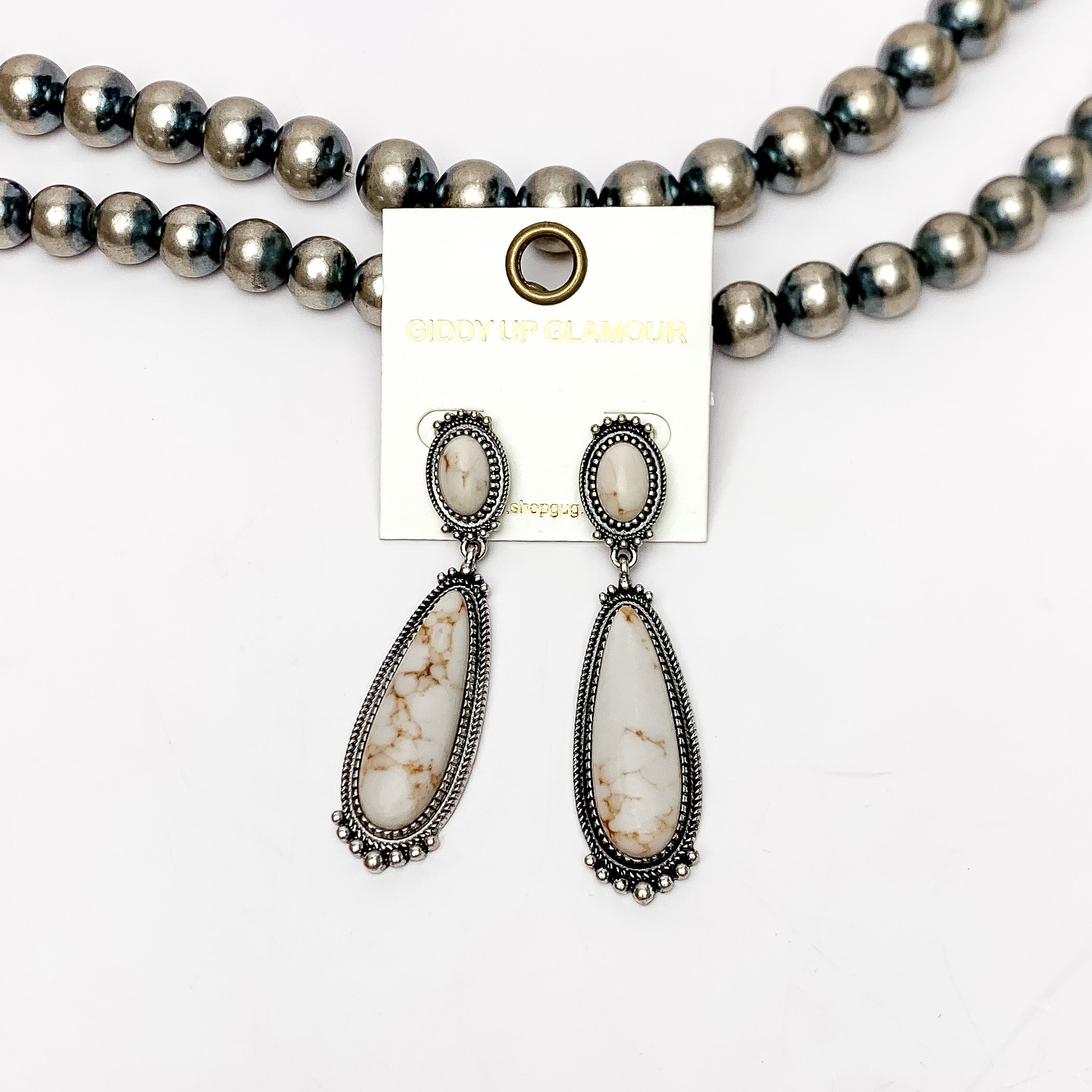 Southern Saturdays Silver Tone Drop Earrings in Ivory. These earrings featured two large stones. The background of the picture is white and the earrings are laying against Navajo pearls.