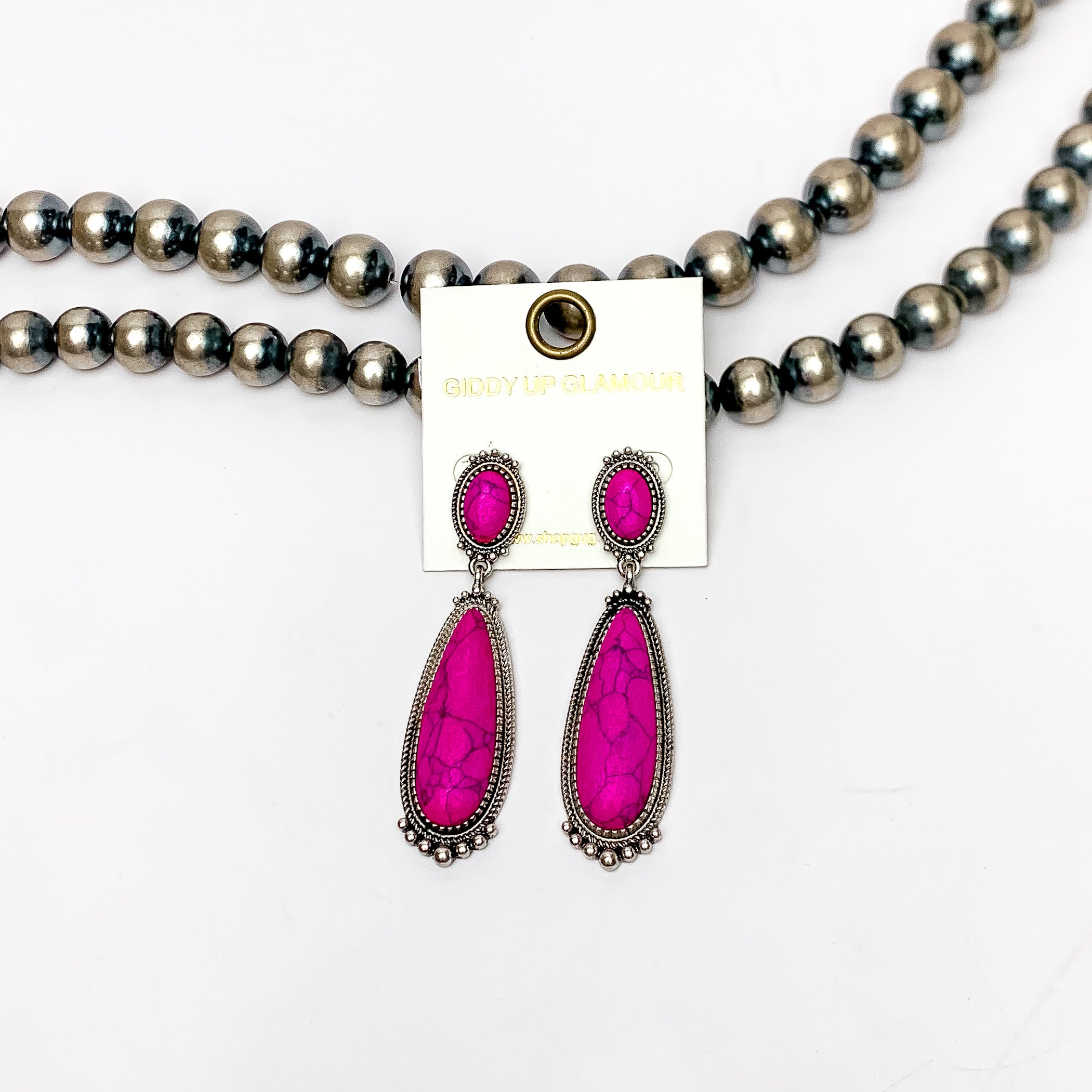 Southern Saturdays Silver Tone Drop Earrings in Hot Pink. These earrings featured two large stones. The background of the picture is white and the earrings are laying against Navajo pearls.