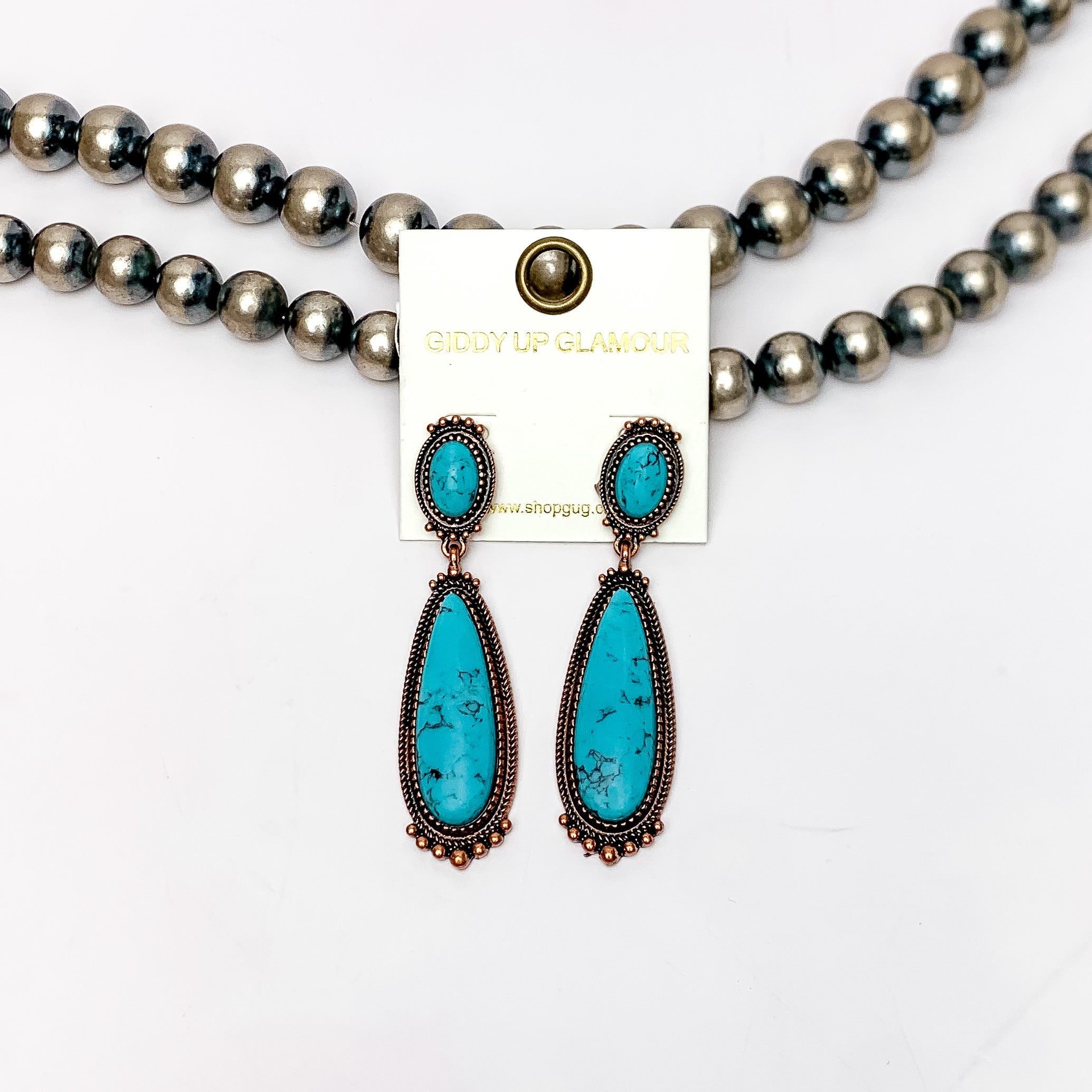 Southern Saturdays Copper Tone Drop Earrings in Turquoise Blue. These earrings featured two large stones. The background of the picture is white and the earrings are laying against Navajo pearls.