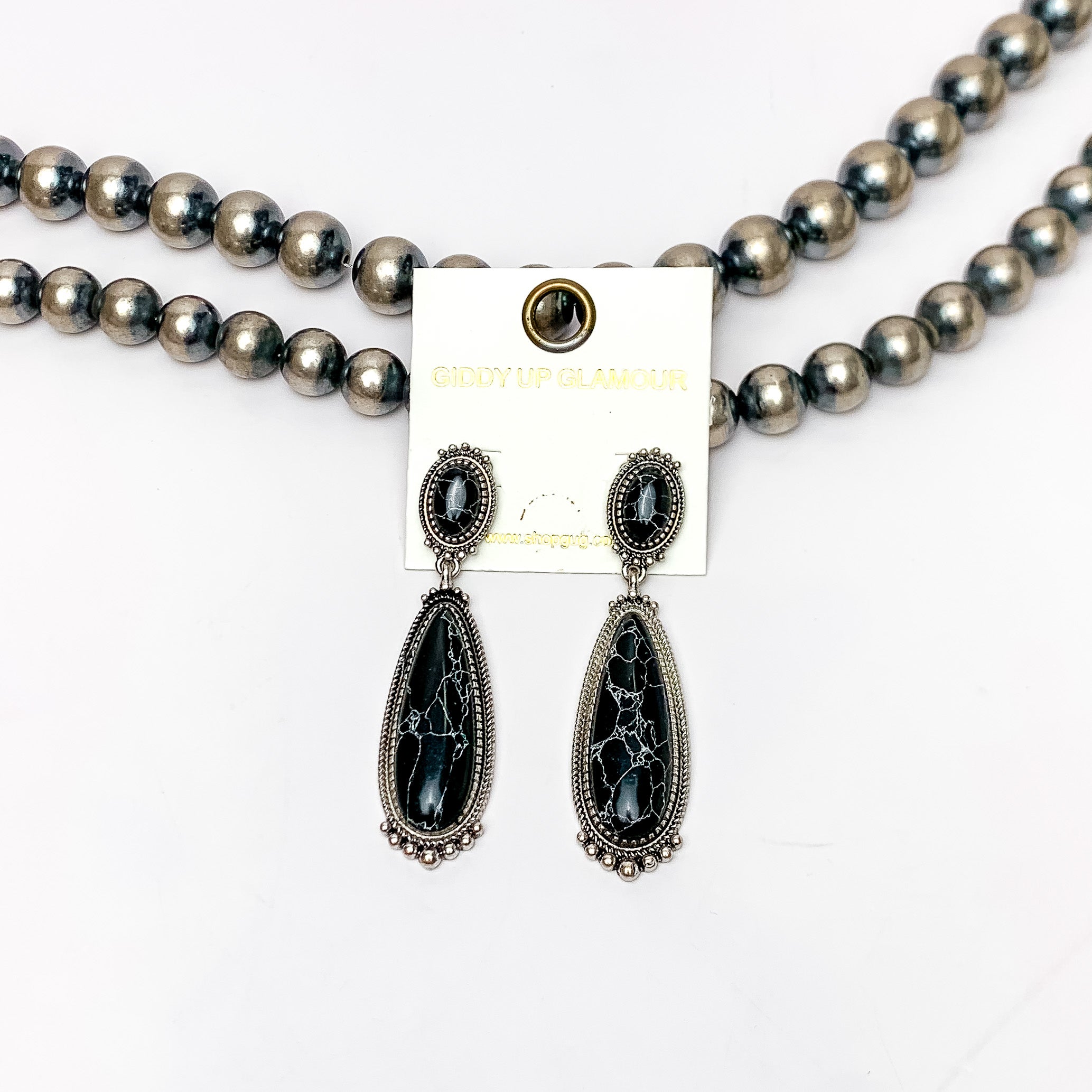 Southern Saturdays Silver Tone Drop Earrings in Black. These earrings featured two large stones. The background of the picture is white and the earrings are laying against Navajo pearls.