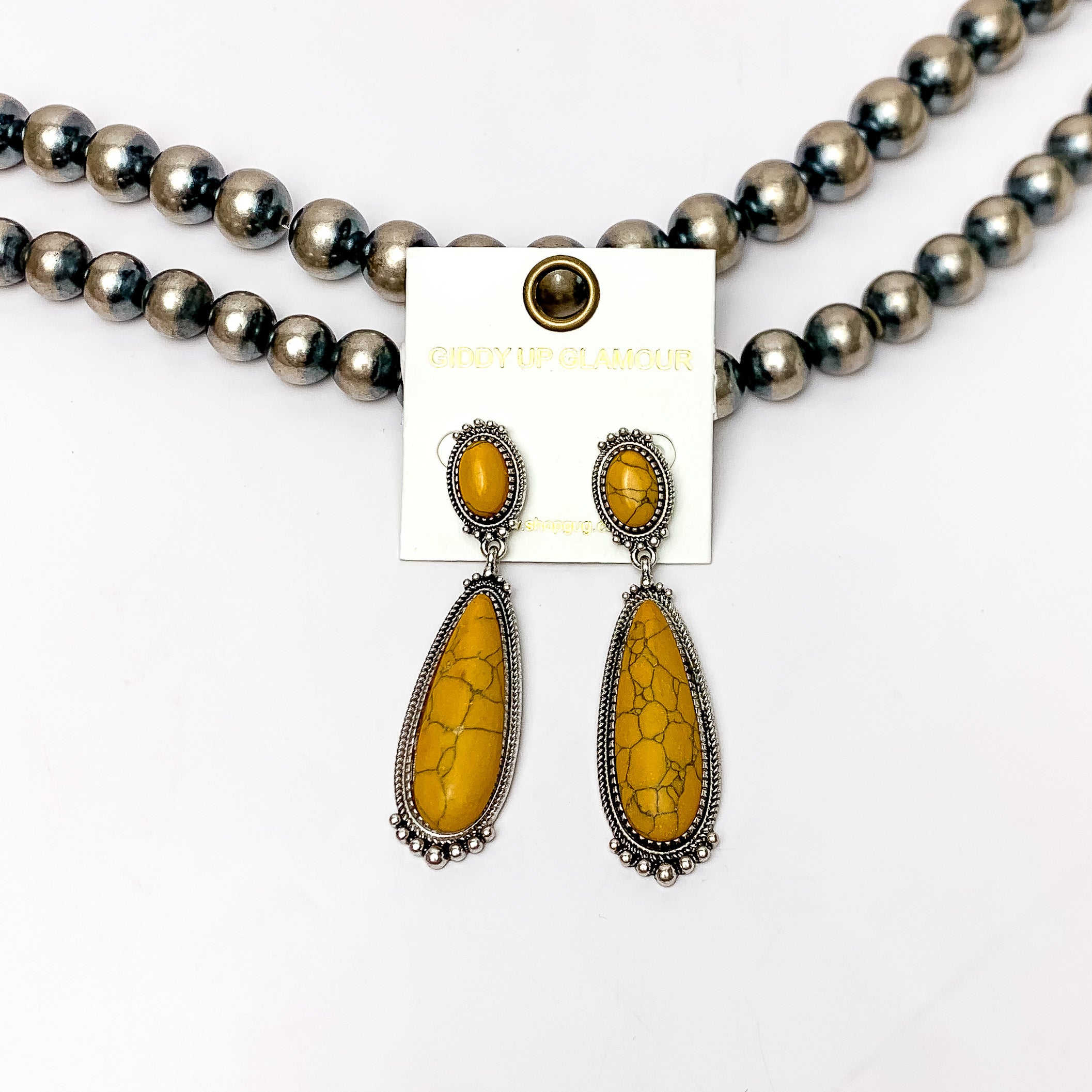 Southern Saturdays Silver Tone Drop Earrings in Yellow. These earrings featured two large stones. The background of the picture is white and the earrings are laying against Navajo pearls.