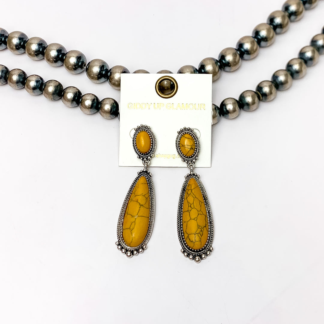 Southern Saturdays Silver Tone Drop Earrings in Yellow. These earrings featured two large stones. The background of the picture is white and the earrings are laying against Navajo pearls.