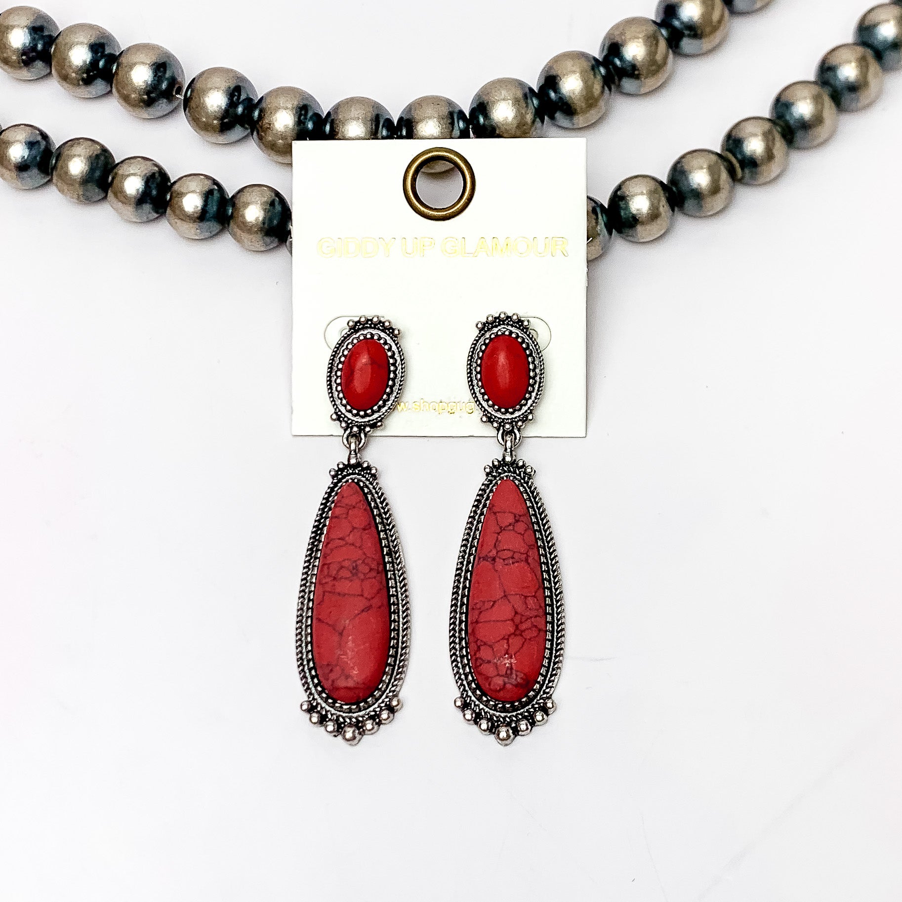 Southern Saturdays Silver Tone Drop Earrings in Red. These earrings featured two large stones. The background of the picture is white and the earrings are laying against Navajo pearls.