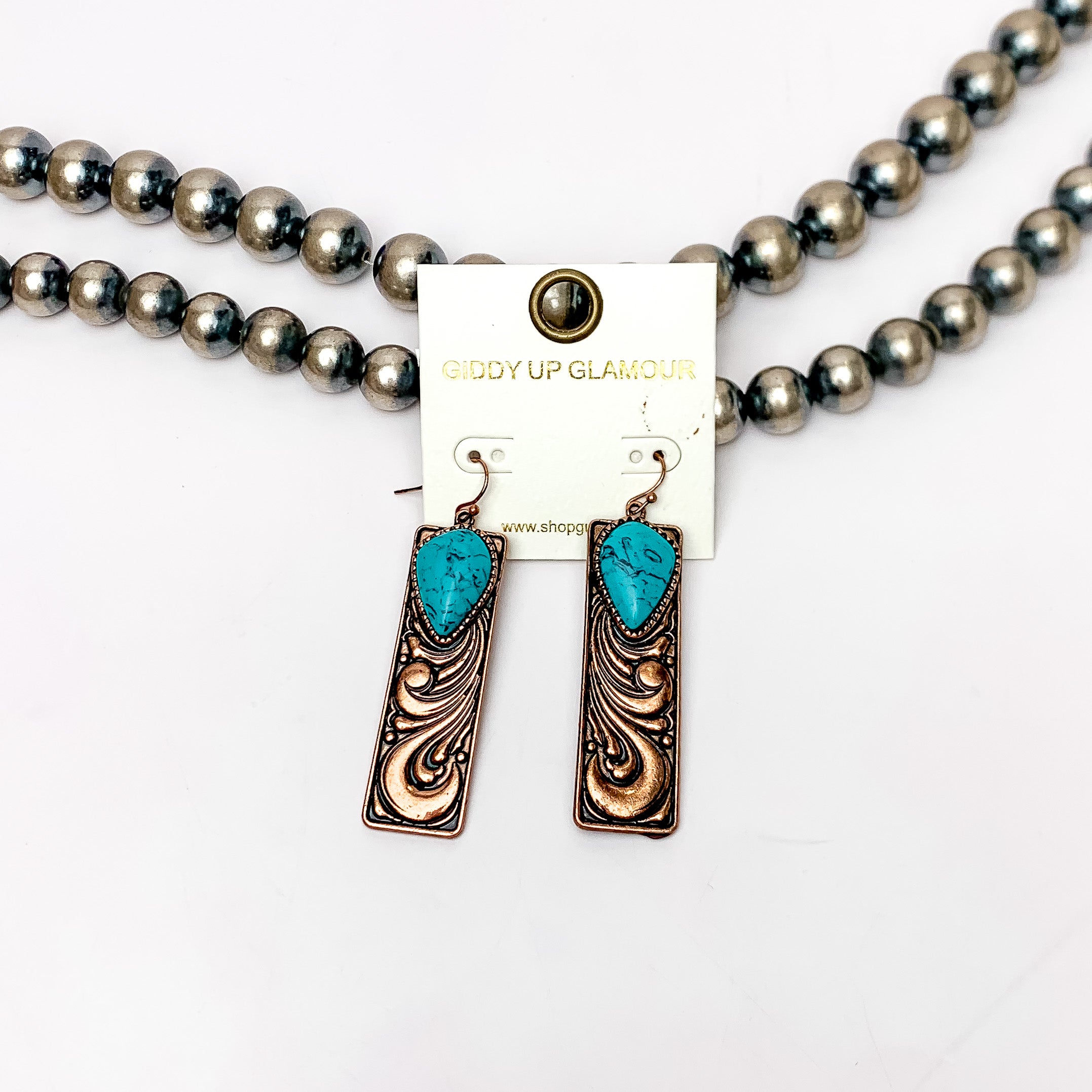 Western Swirl Copper tone Rectangular Earrings With Turquoise Blue Stone. Pictured on a white background with Navajo beads behind the earrings.