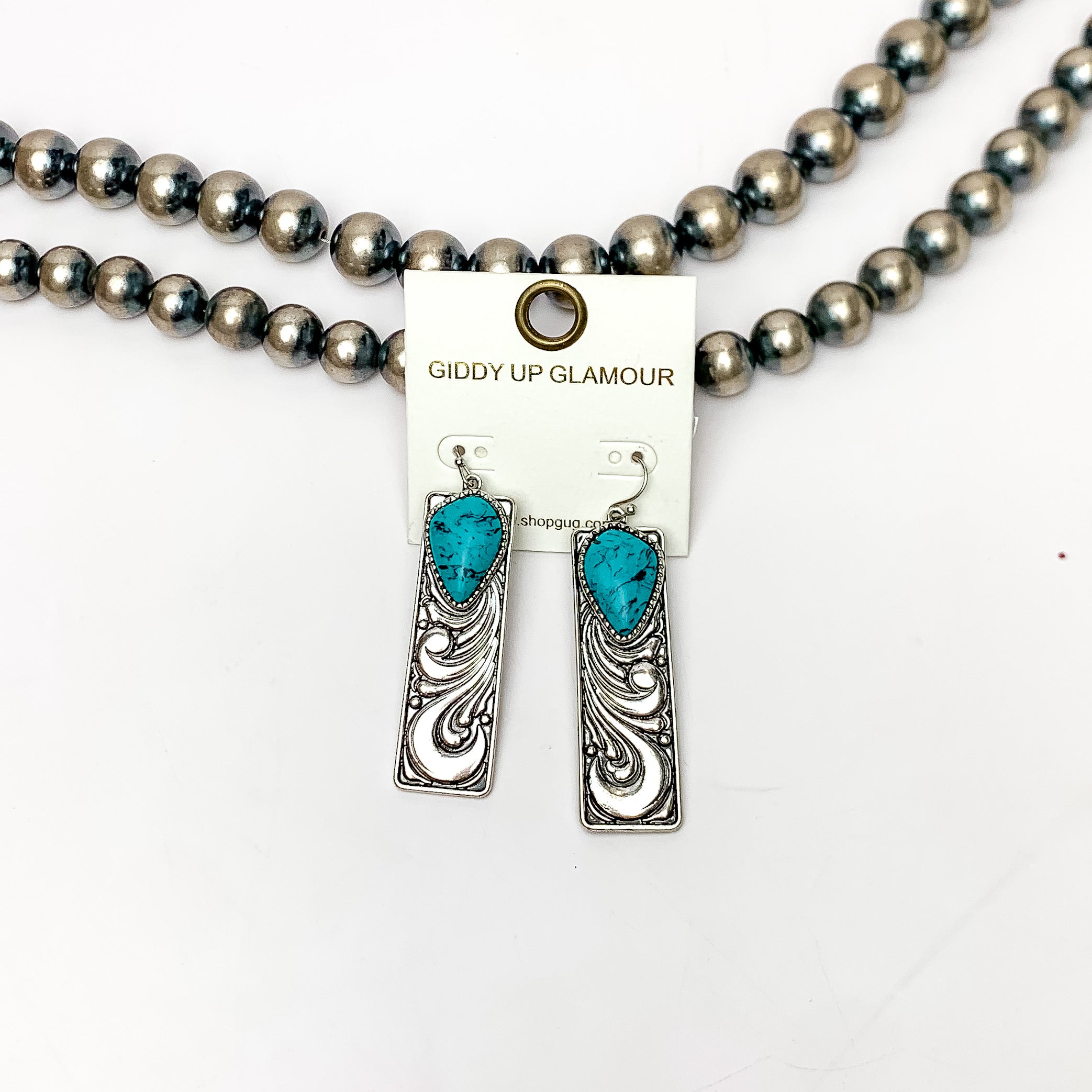 Western Swirl Silver tone Rectangular Earrings With Turquoise Blue Stone. Pictured on a white background with Navajo beads behind the earrings.