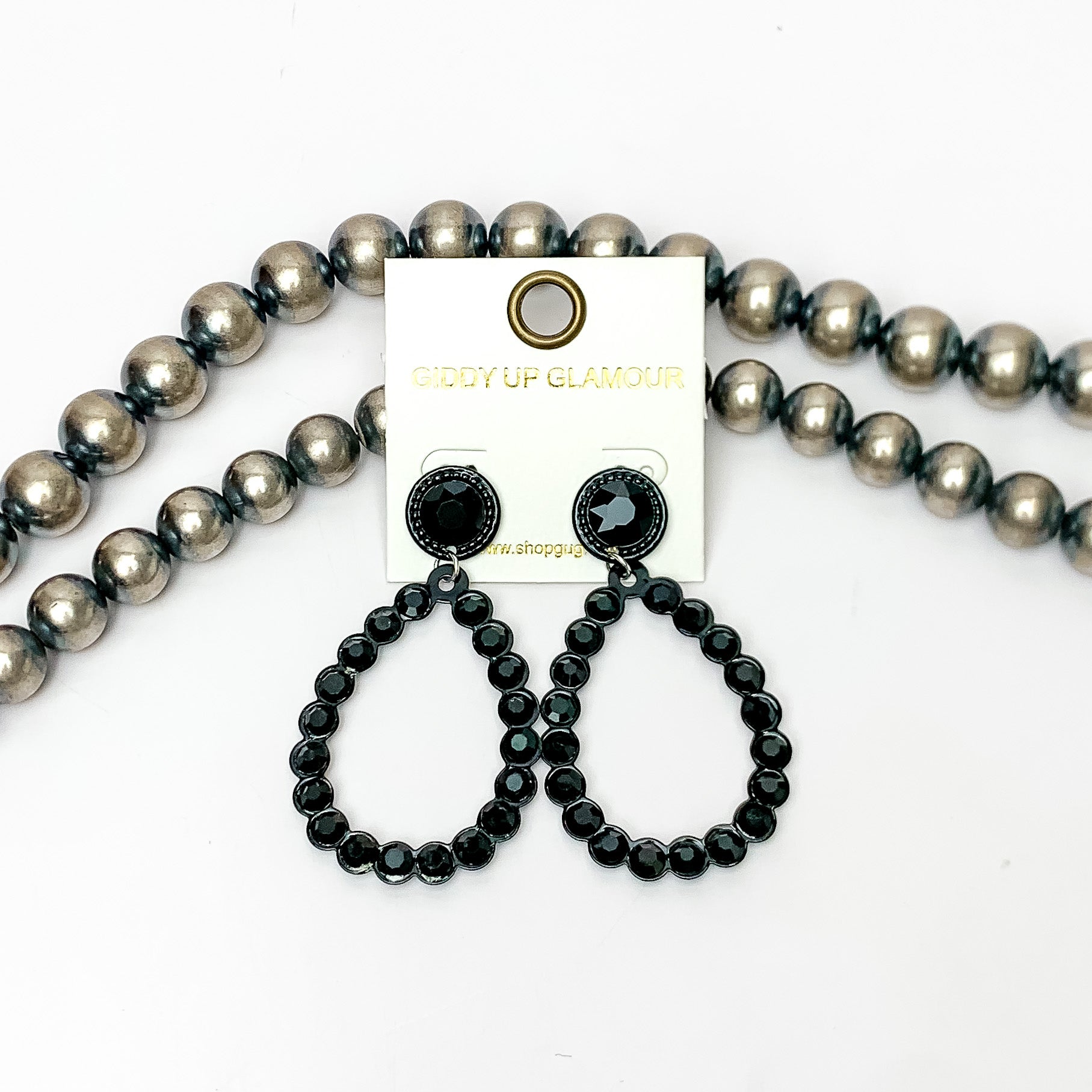 Glitzy Girl Black Crystal Teardrop Earrings in Black. Pictured on a white background with Navajo pearls behind the earrings.