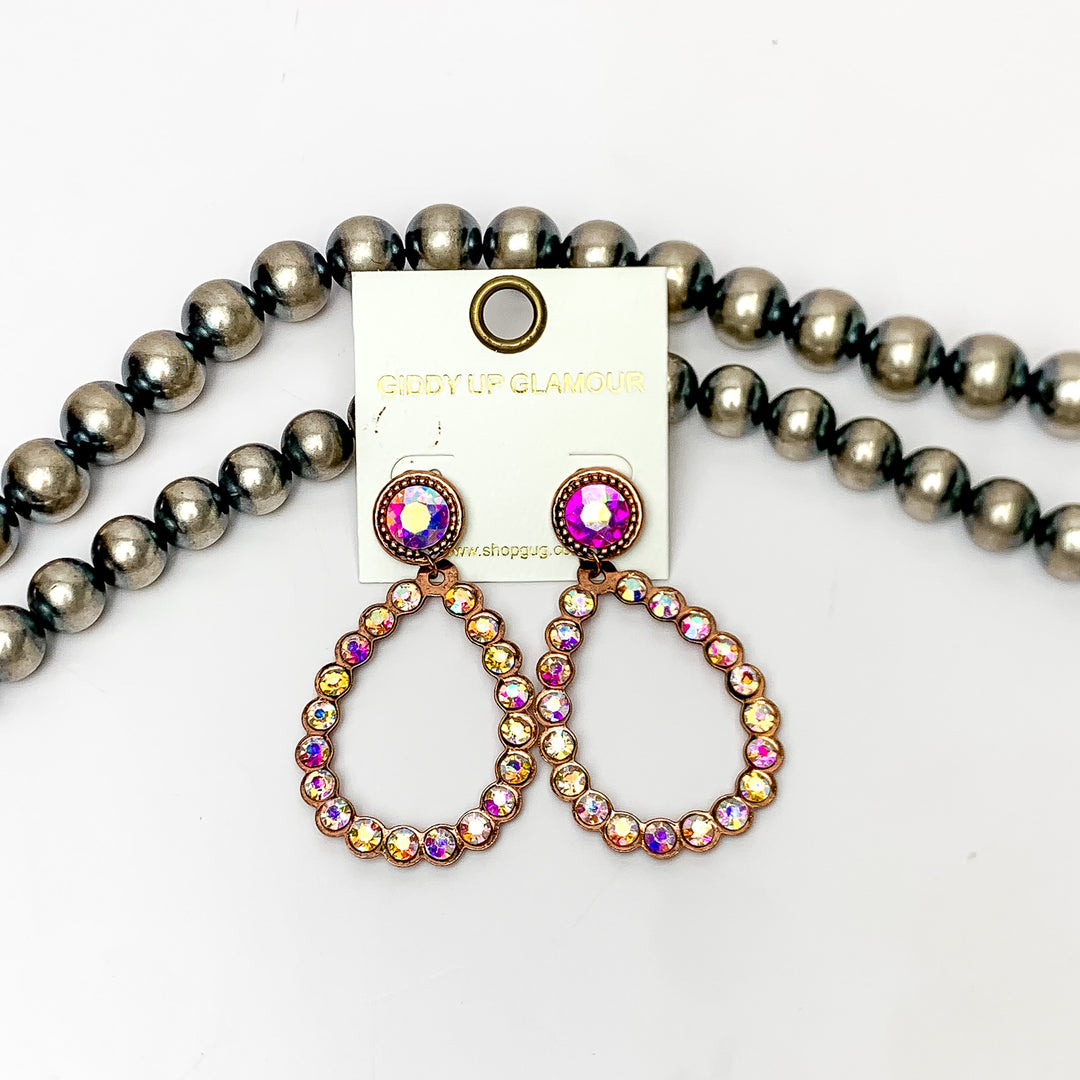 Glitzy Girl AB Crystal Teardrop Earrings in Copper Tone. Pictured on a white background with Navajo pearls behind the earrings.