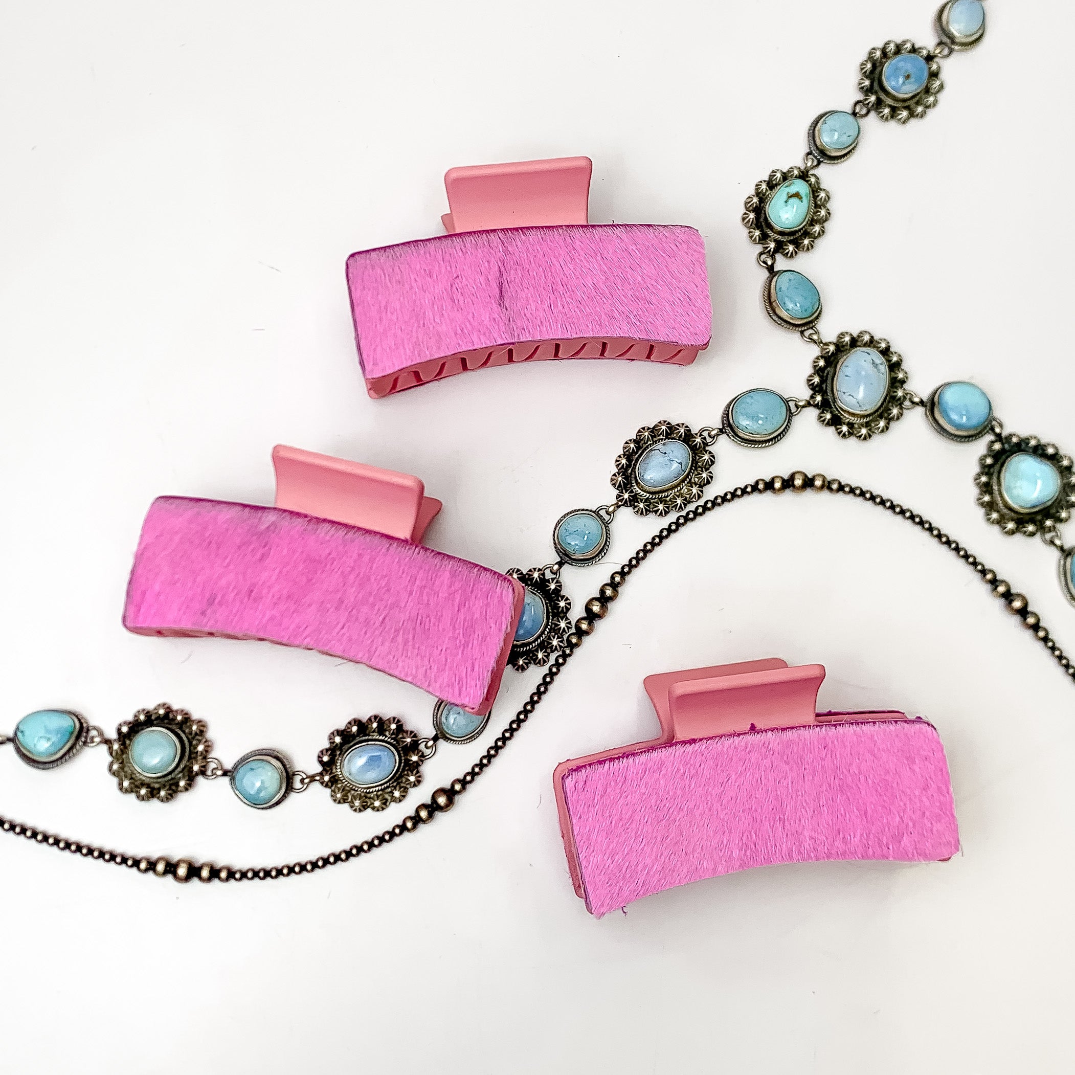 Pictured are three pink hair clips with light pink hide patches. These earrings are pictured on a white background with silver necklaces under the clips. 