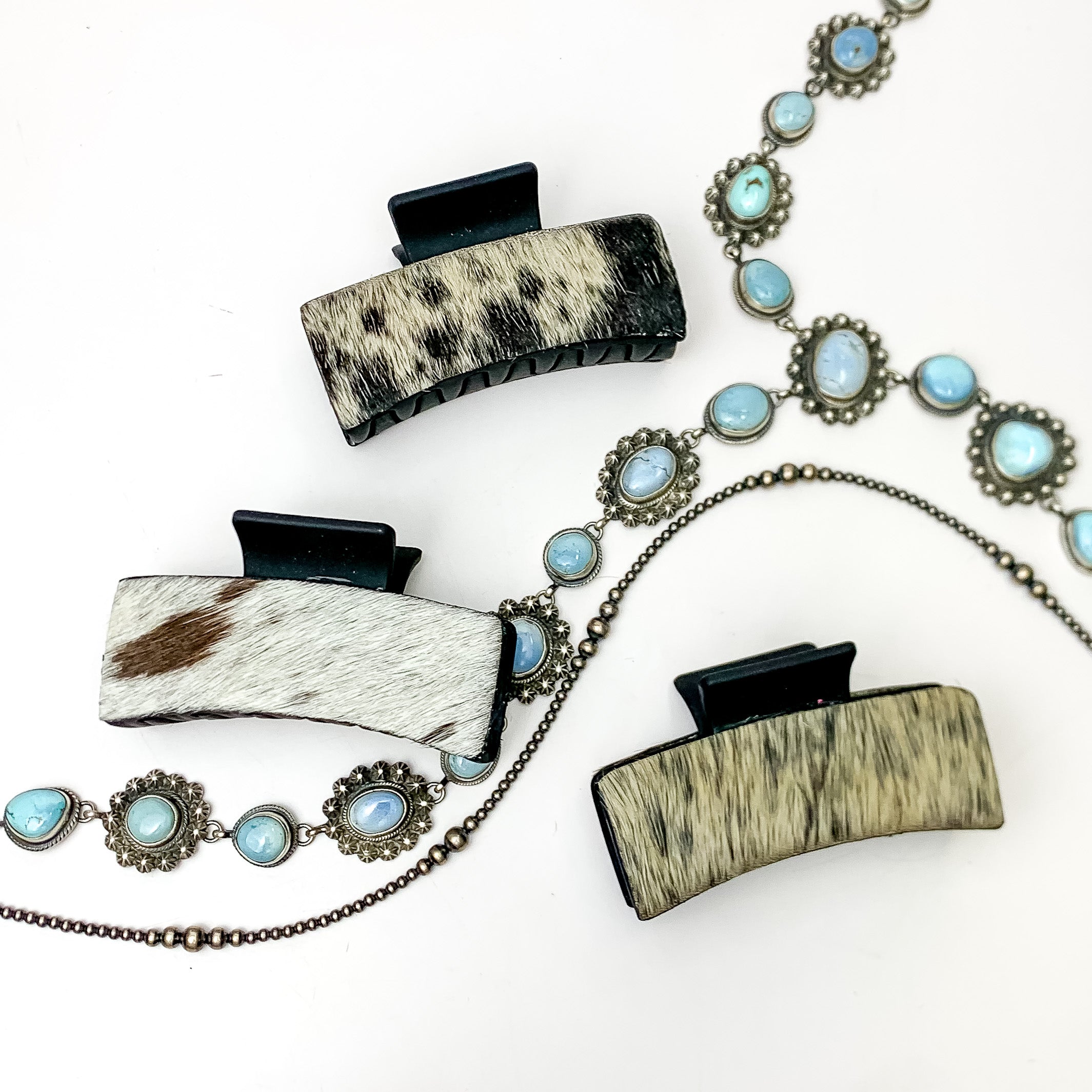 Pictured are three black hair clips with ivory and black mix hide patches. These earrings are pictured on a white background with silver necklaces under the clips. 