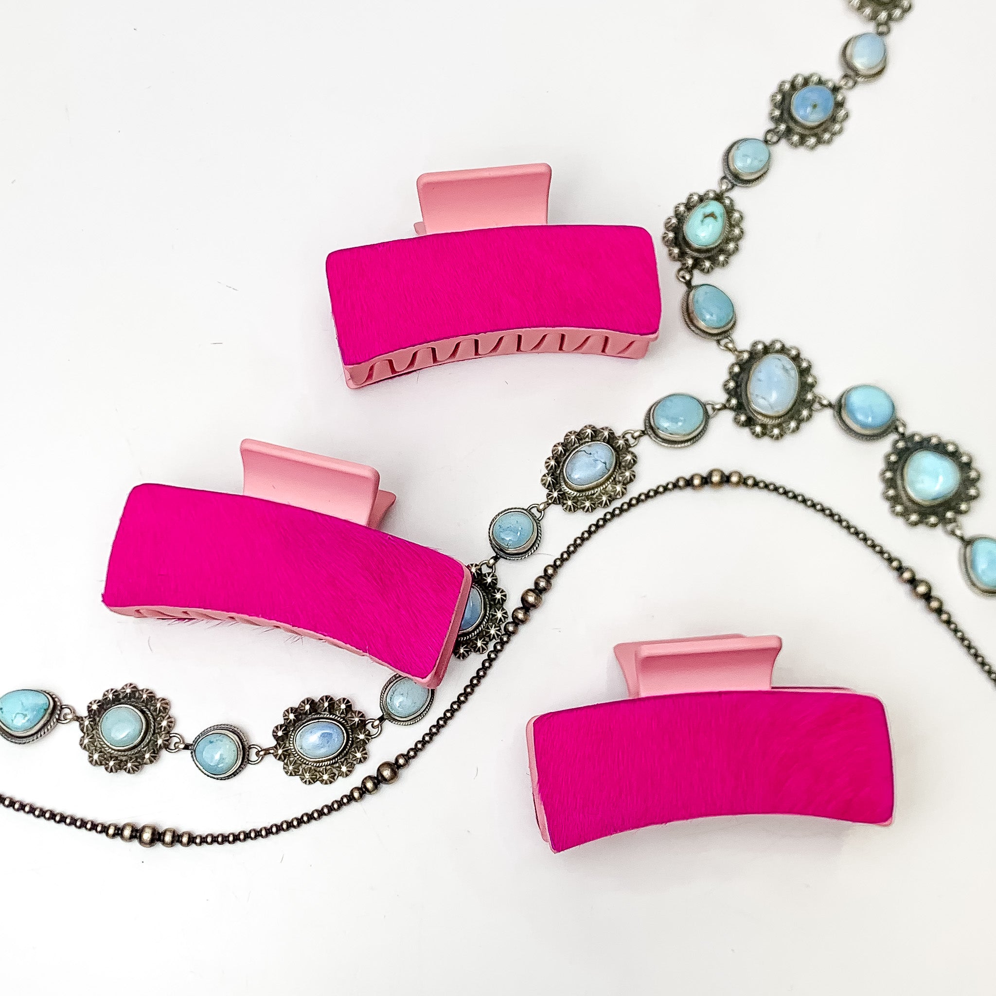 Pictured are three pink hair clips with hot pink hide patches. These earrings are pictured on a white background with silver necklaces under the clips. 