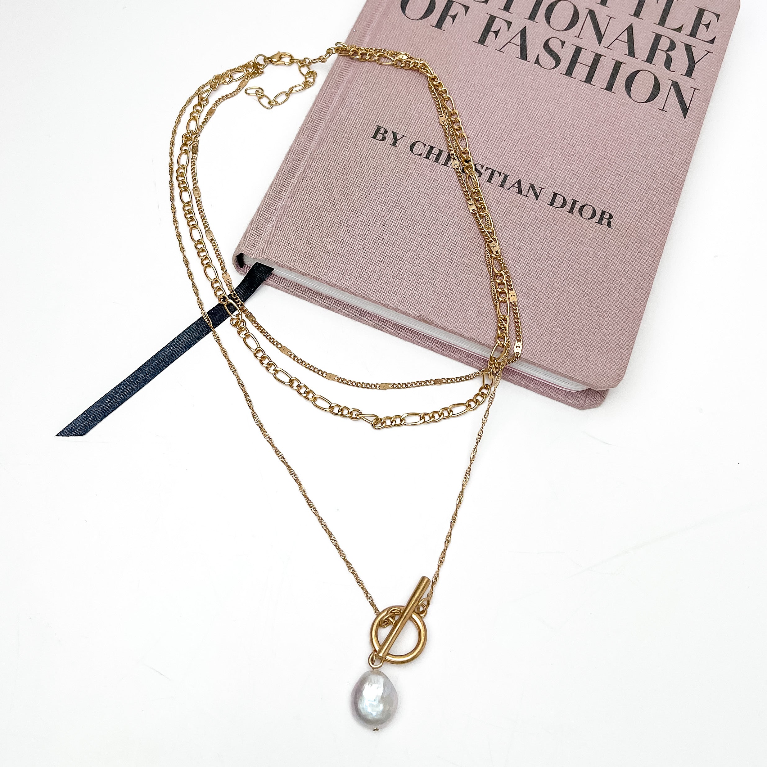 Pretty as a Pearl Gold Tone Chain Necklace. Pictured on a white background with part of the necklace laying on a pink book.