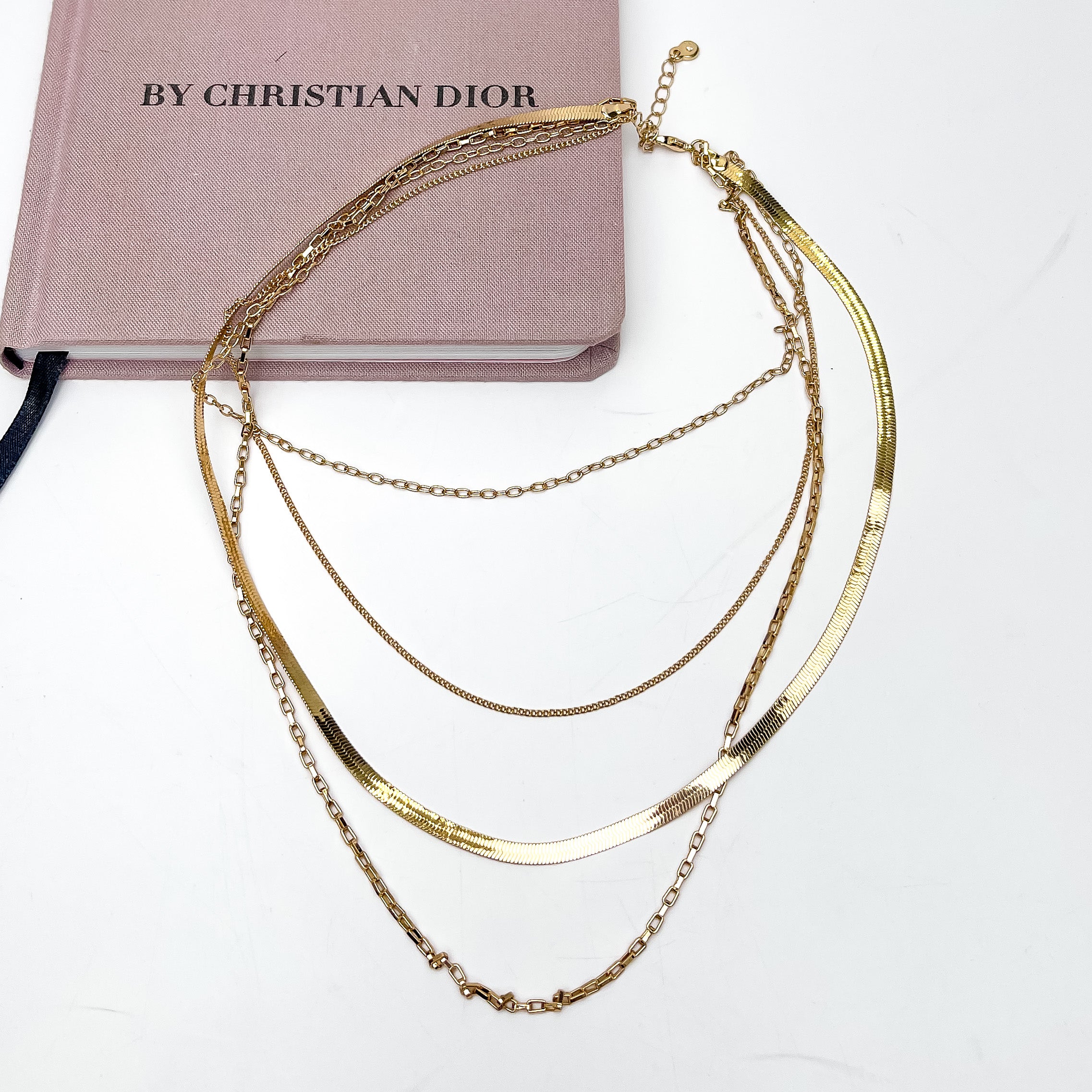 Memorable Moment Multi Strand Gold Tone Necklace. This necklace is partly on a pink book with a white background.