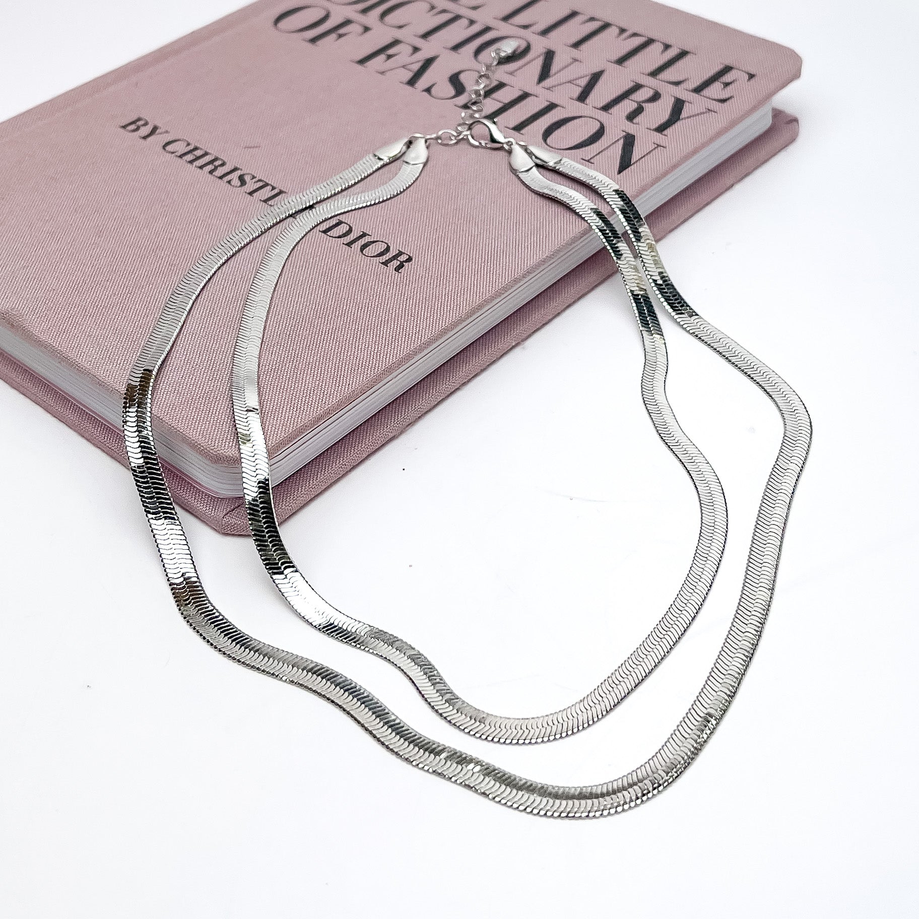 Night Life Double layered Silver Tone Chain Necklace. The necklace is pictured on a white background with part of it on a pink book.