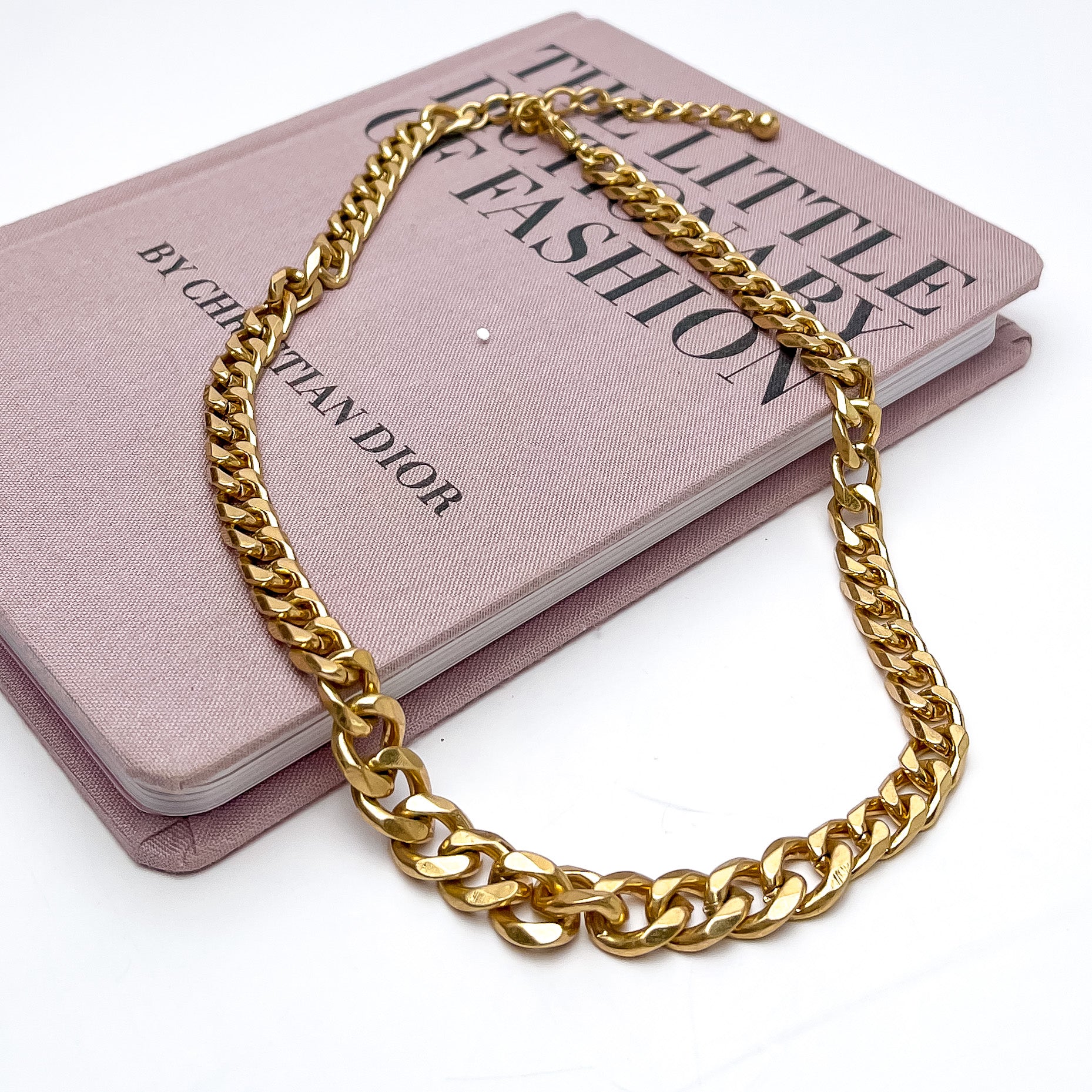 Go to Gold Tone Chain Necklace. This necklace is on a pink book with a white background.