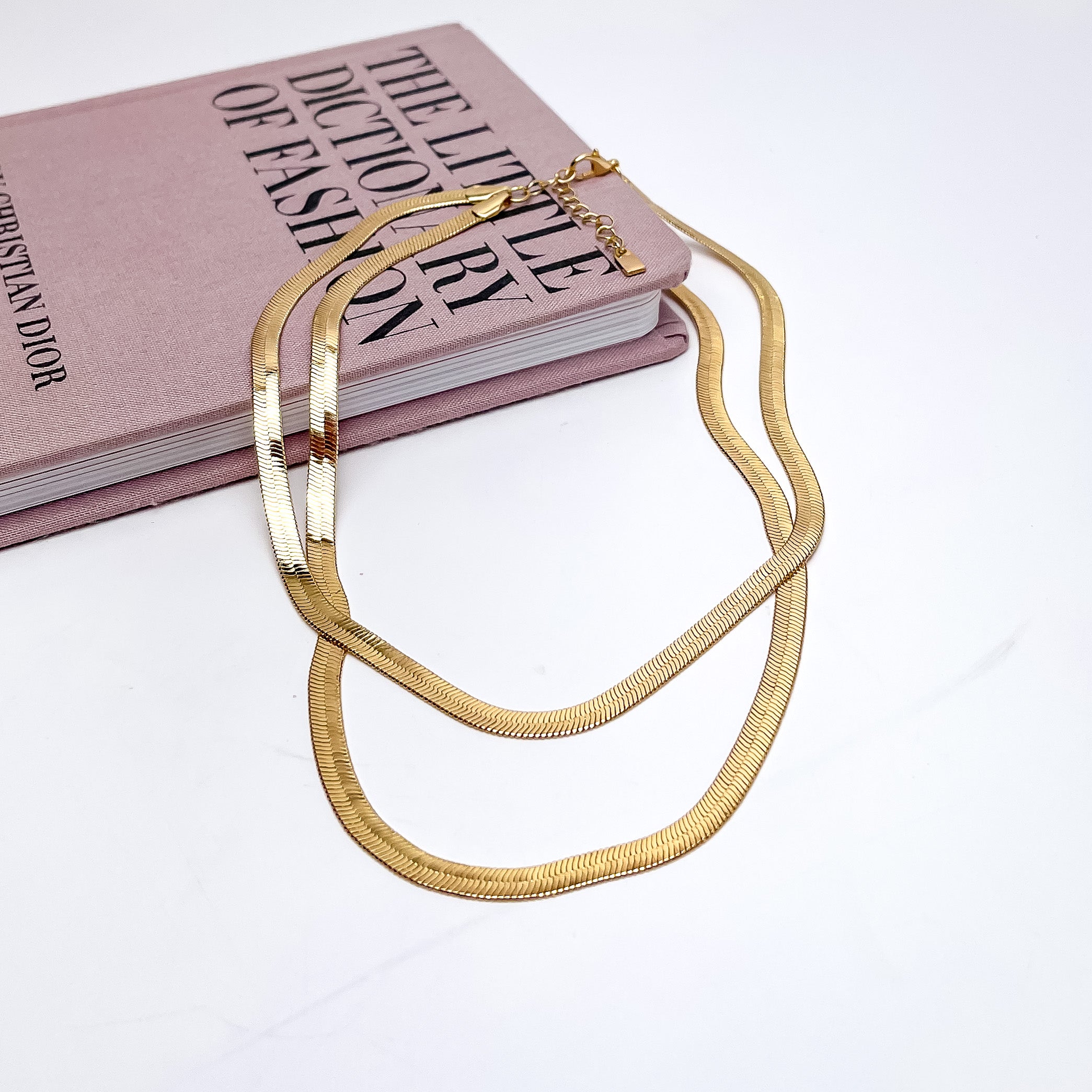 Night Life Double layered Gold Tone Chain Necklace. the necklace is pictured on a white background with part of it on a pink book.