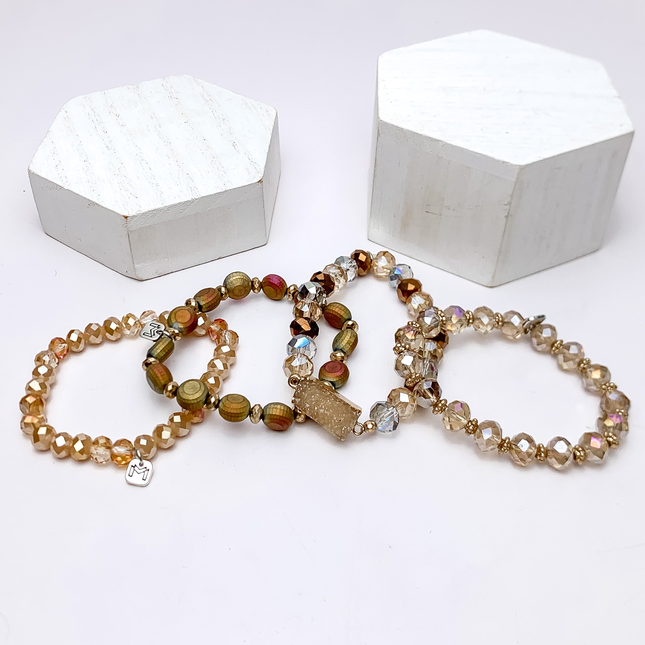 Set of Four | Crystal Beaded Bracelet Set in Gold Tones. These bracecelts are pictured on a white background with two white podiums behind them.