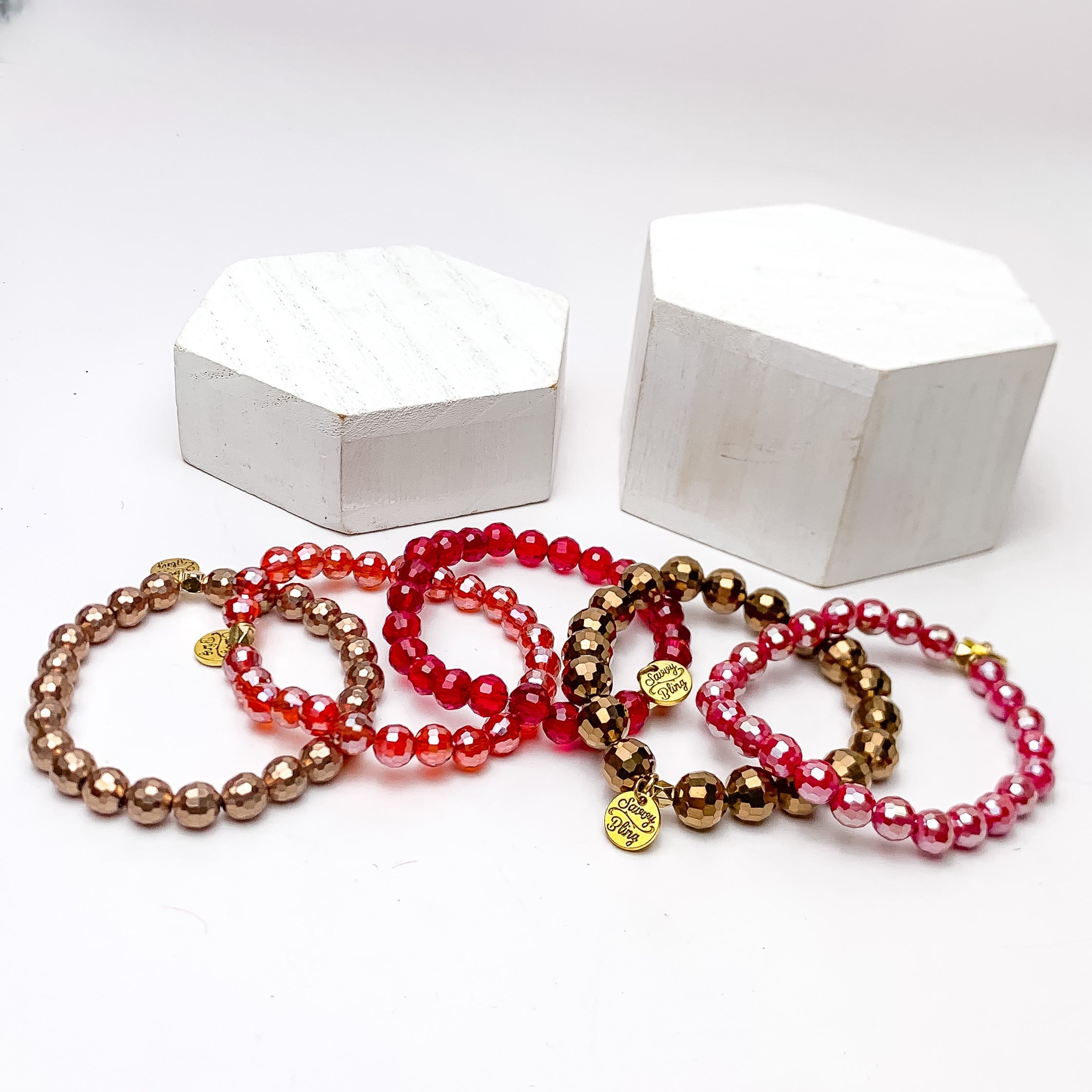 Set of Five | All Nighter Crystal Beaded Bracelet Set in Red and Gold Tones. These bracelets are pictured on a white background with two white podiums behind them.