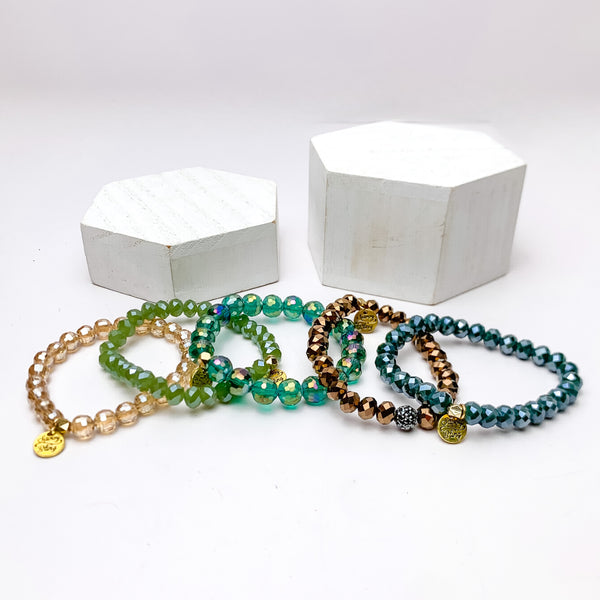 Set of Five | All Nighter Crystal Beaded Bracelet Set in Turquoise Blue and Gold Tones. These bracelets are pictured on a white background with two white podiums behind them.