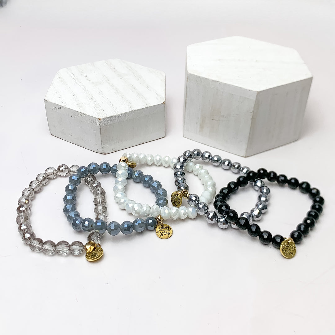 Set of Five | All Nighter Crystal Beaded Bracelet Set in Grey, Black, and White. These bracelets are pictured on a white background with two white podiums behind them.