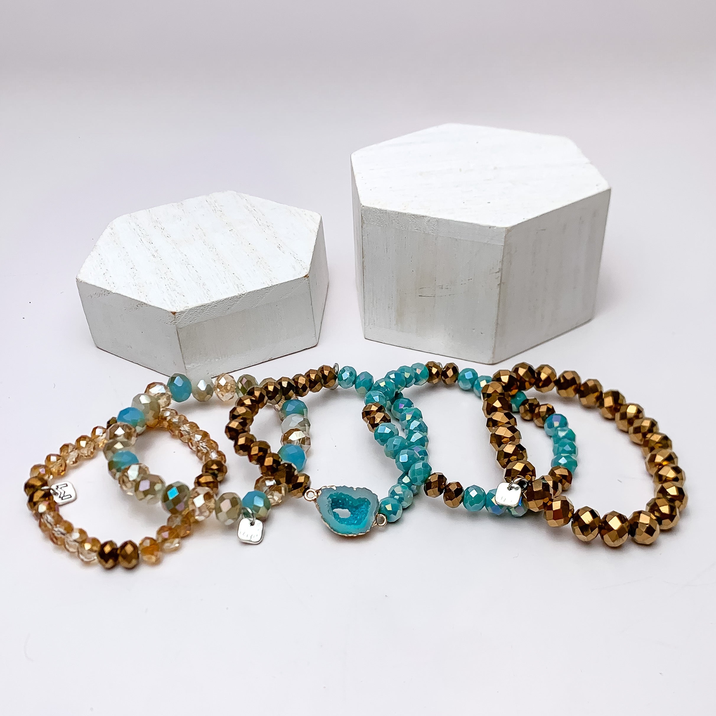 Set of Five | All Nighter Crystal Beaded Bracelet Set in Turquoise Blue and Gold Tones. These bracelets are pictured on a white background with two white podiums behind them.