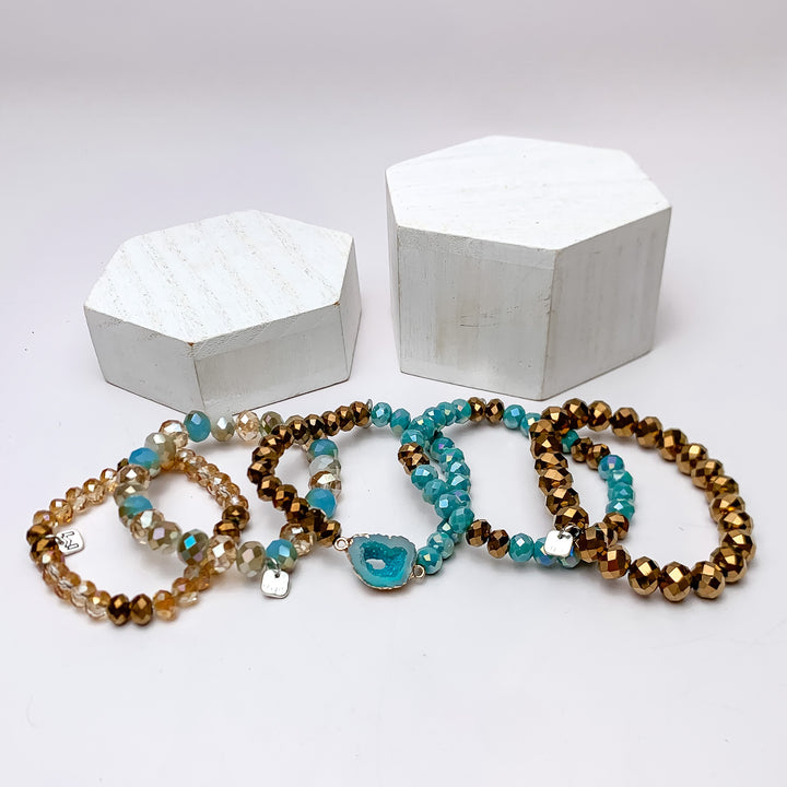Set of Five | All Nighter Crystal Beaded Bracelet Set in Turquoise Blue and Gold Tones. These bracelets are pictured on a white background with two white podiums behind them.