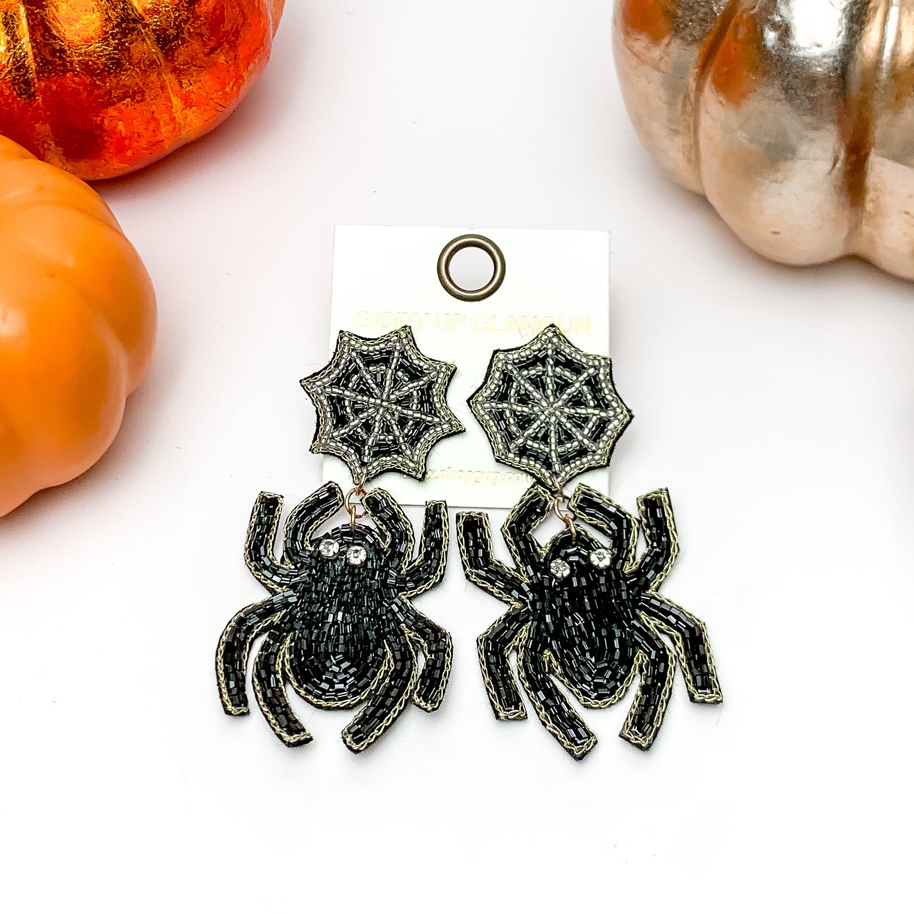 Beaded Spider Earrings With Web Post in Black. These earrings are on a white background with orange and silver pumpkins around them.