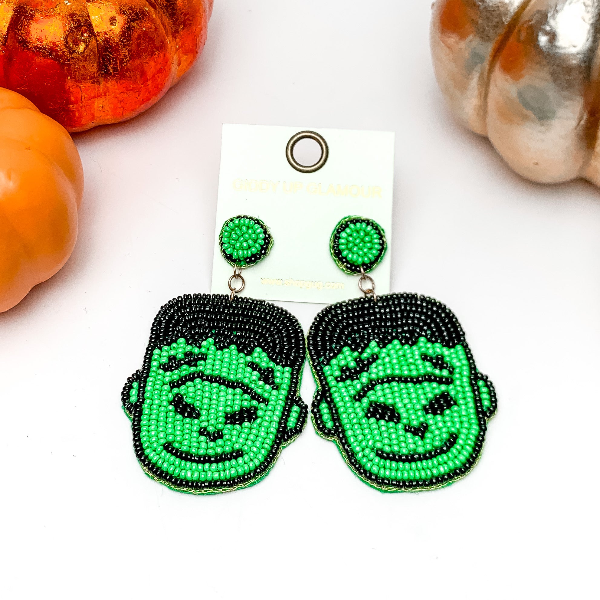 Beaded Frankenstein Earrings in Green, and Black. These earrings are on a white background with orange and silver pumpkins around them.