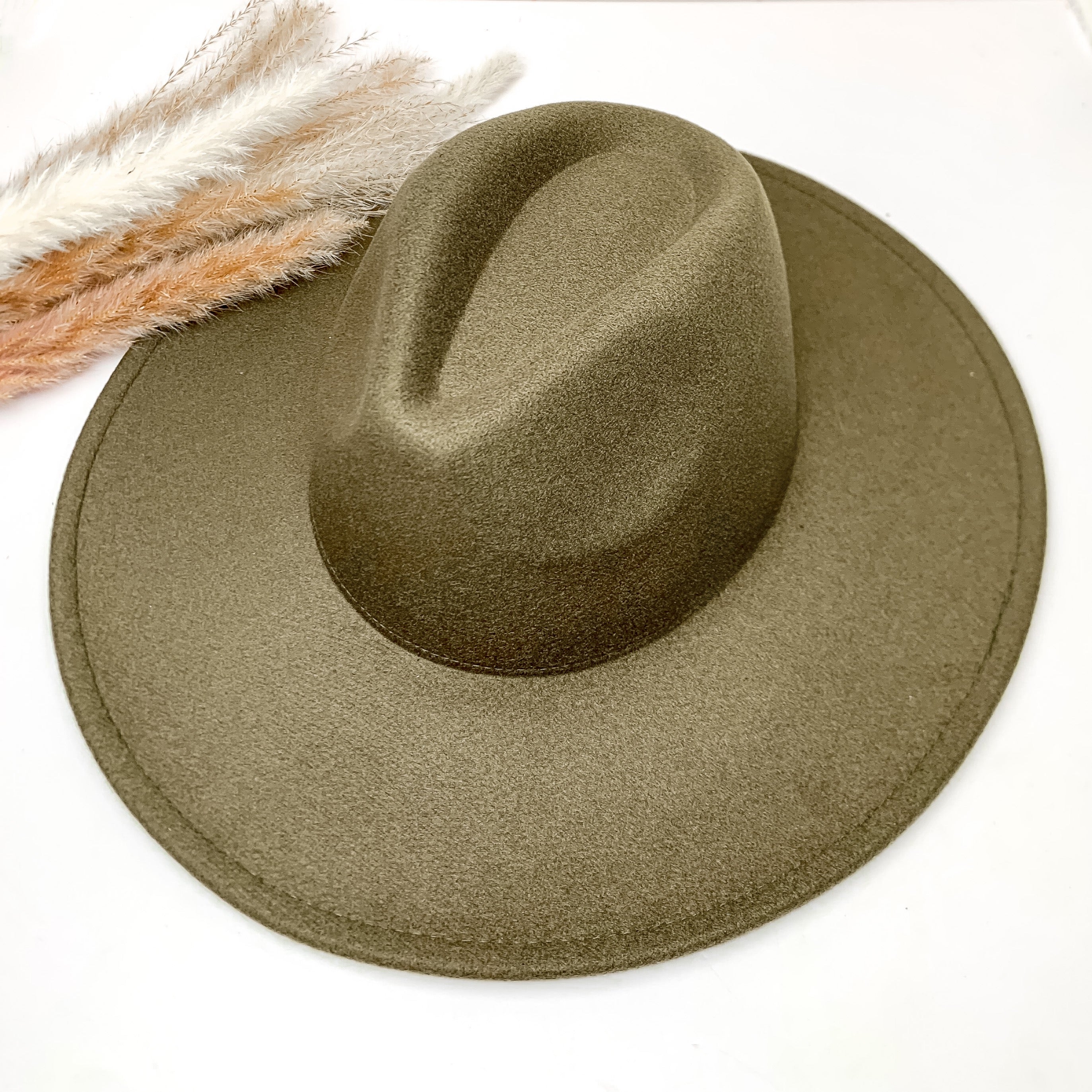 Plain and simple faux felt hat in olive green color. This hat is sitting on a white background. There is brown and white feathers to the left of the hat.