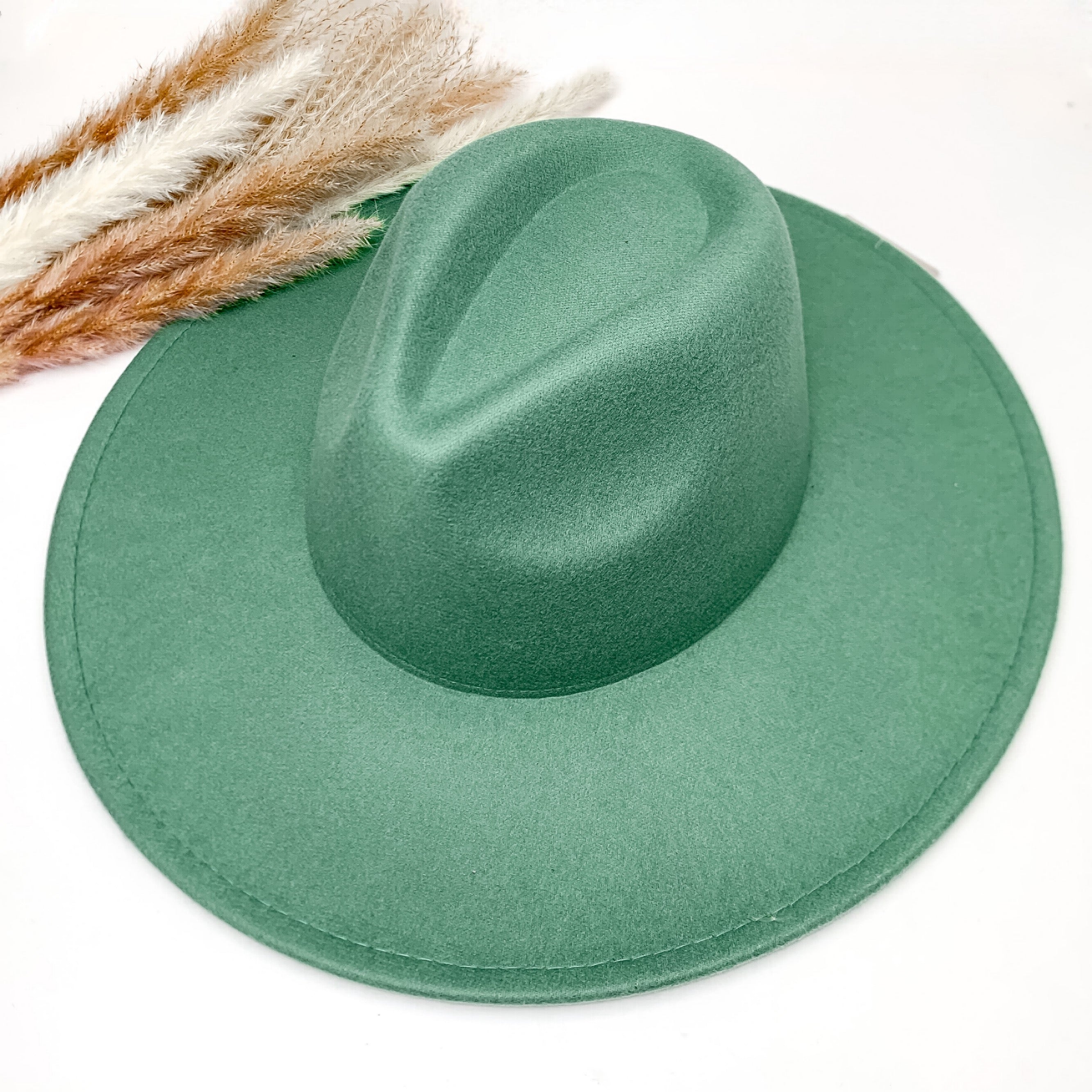 Plain and simple faux felt hat in turquoise green color. This hat is sitting on a white background. There is brown and white feathers to the left of the hat.