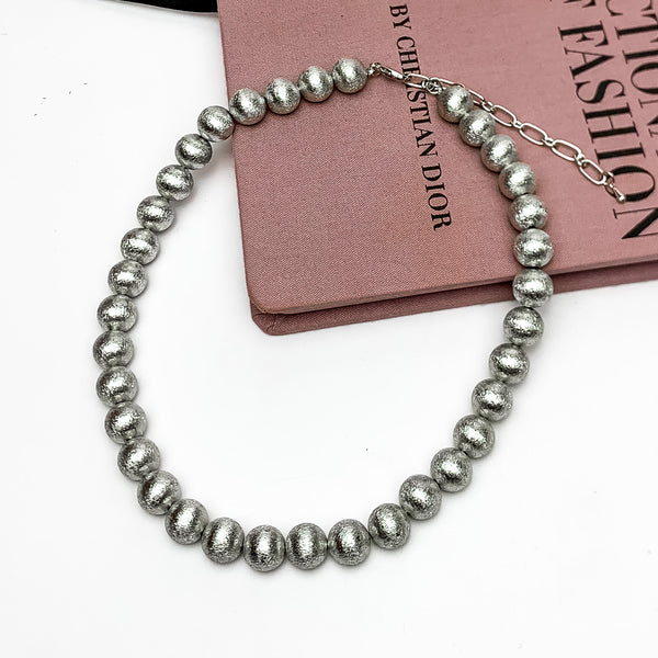 Smaller silver tone beaded necklace. Shiny silver coloring. This necklace is on a pink book with a white background.