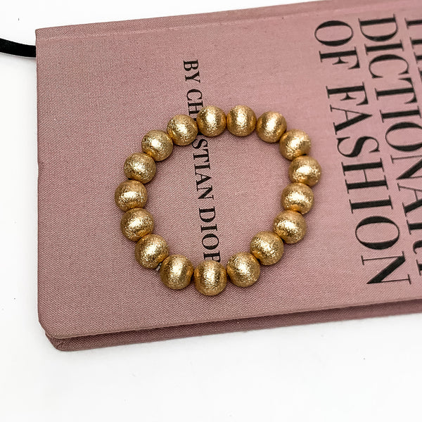 Medium gold tone beaded bracelets. This bracelet is pictured on a pink book with a white background.